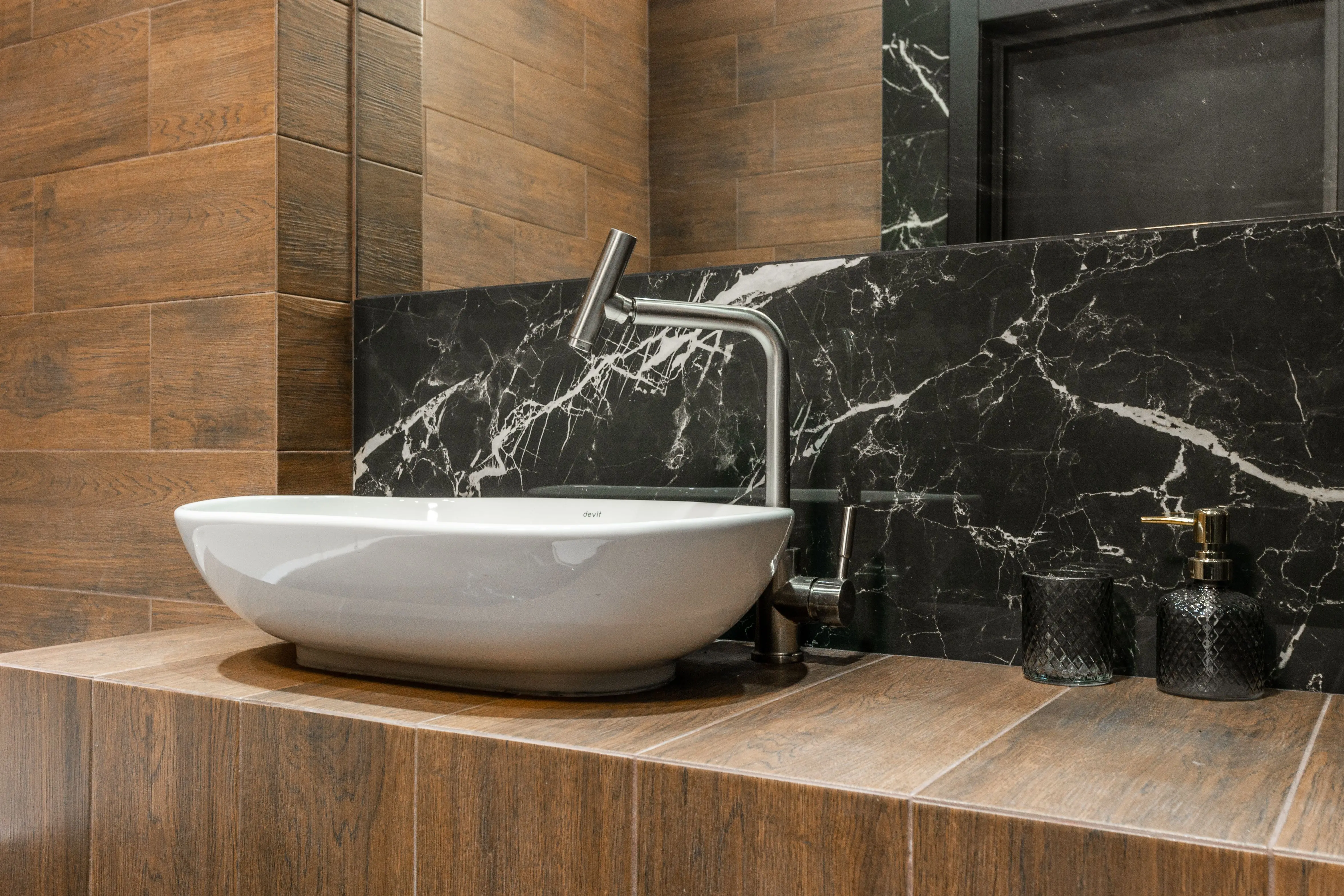 black backsplash Detail of interior design of contemporary home bathroom with white sink and chrome tap on wood like tiled counter near wall with mirror and marble tiles