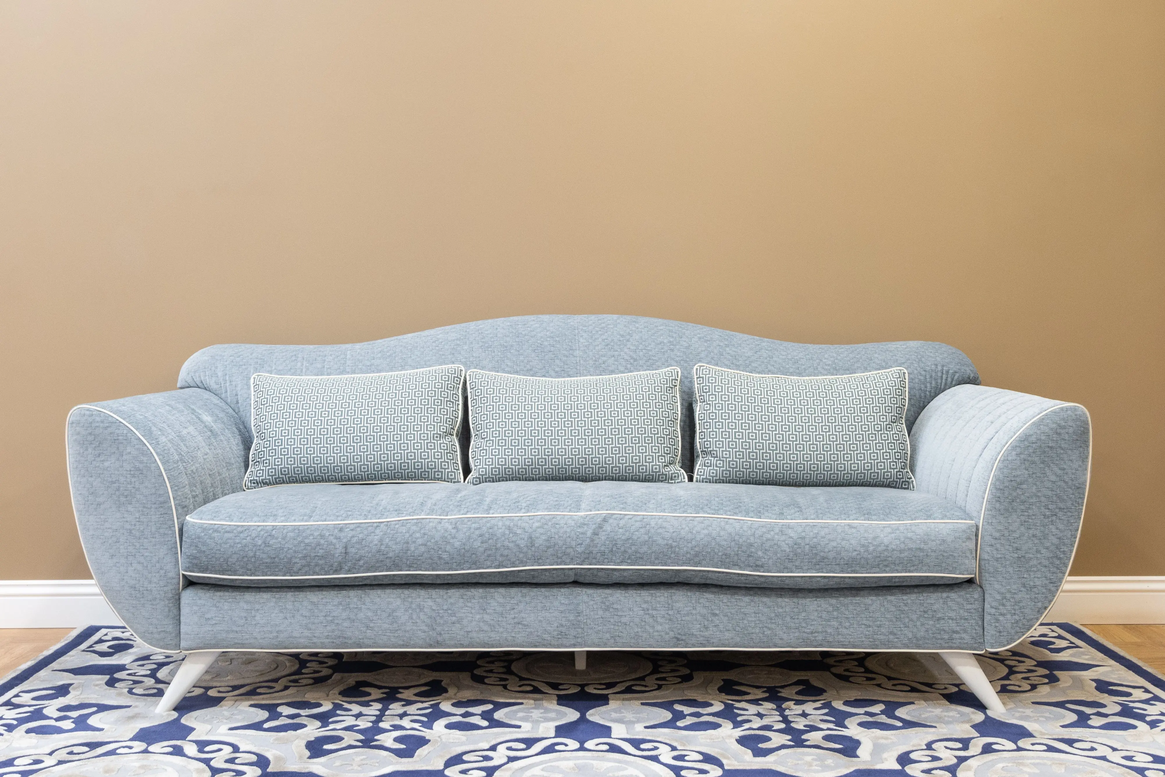 blue decorative pillows Stylish blue sofa with cushions on patterned carpet, perfect for a modern, cozy living space.