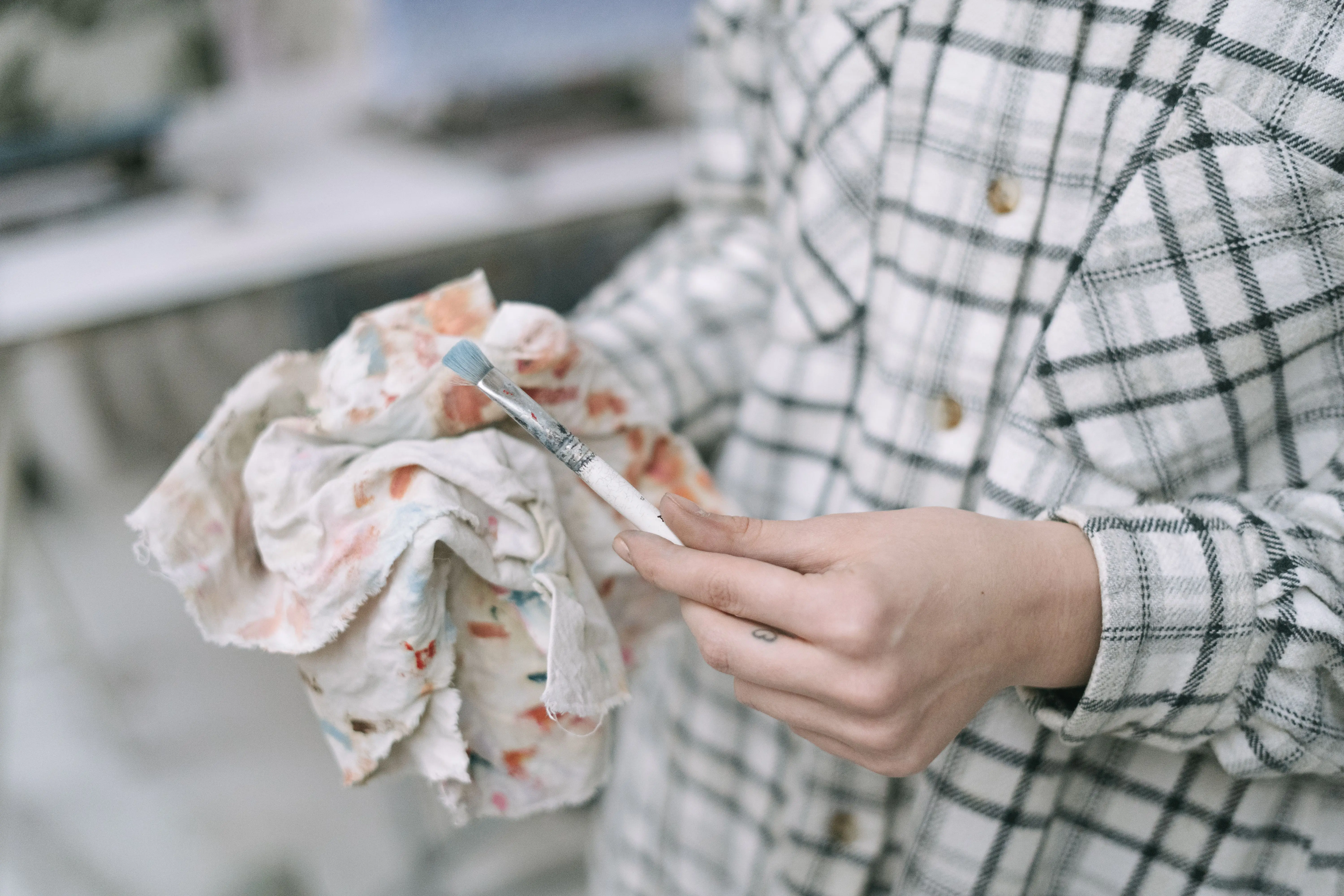 white stain Close-up image of an artist in plaid shirt cleaning a paintbrush with a colorful cloth