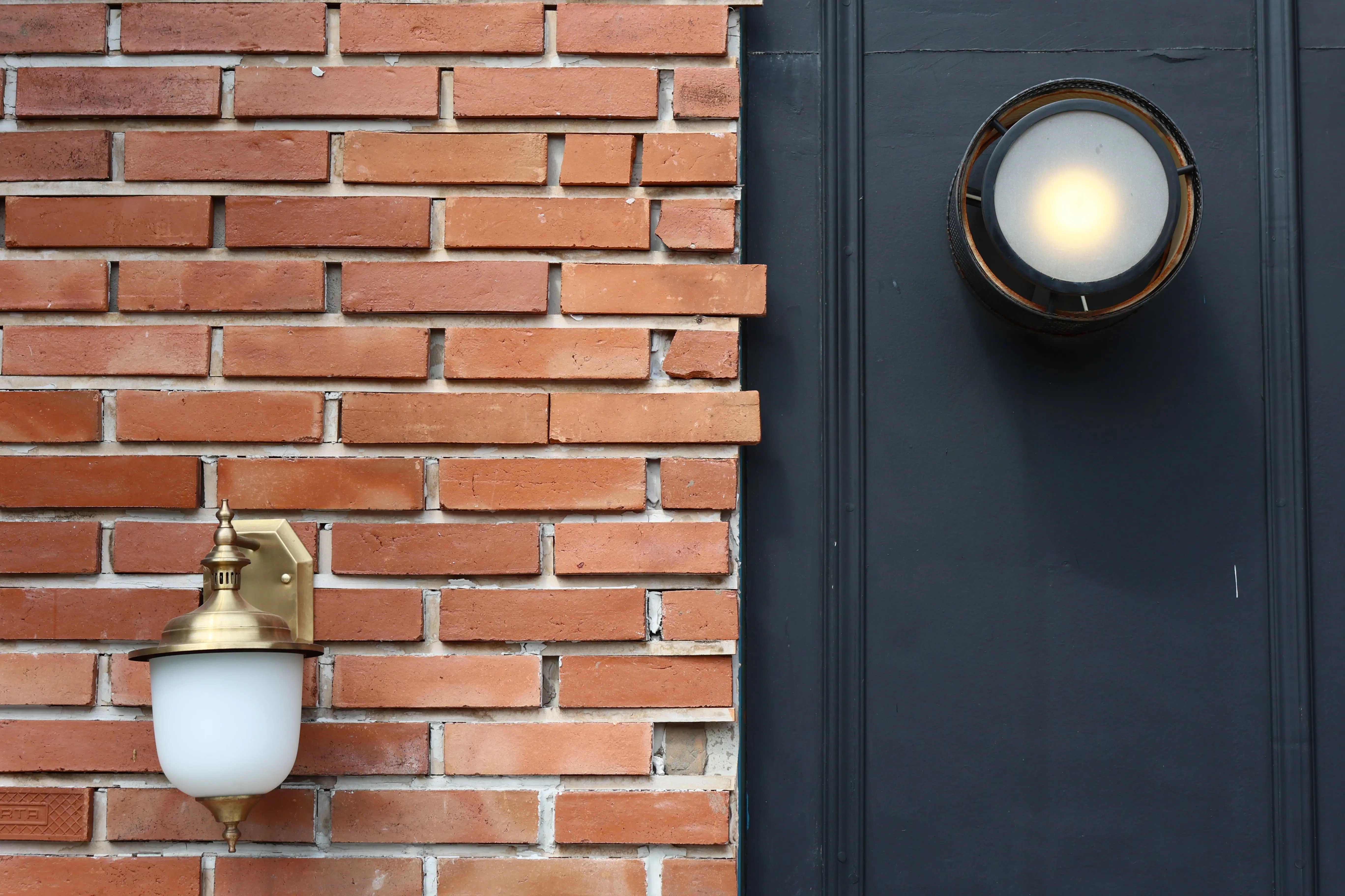 sconce outdoor wall light A rustic brick wall featuring two modern outdoor light fixtures, creating visual contrast.