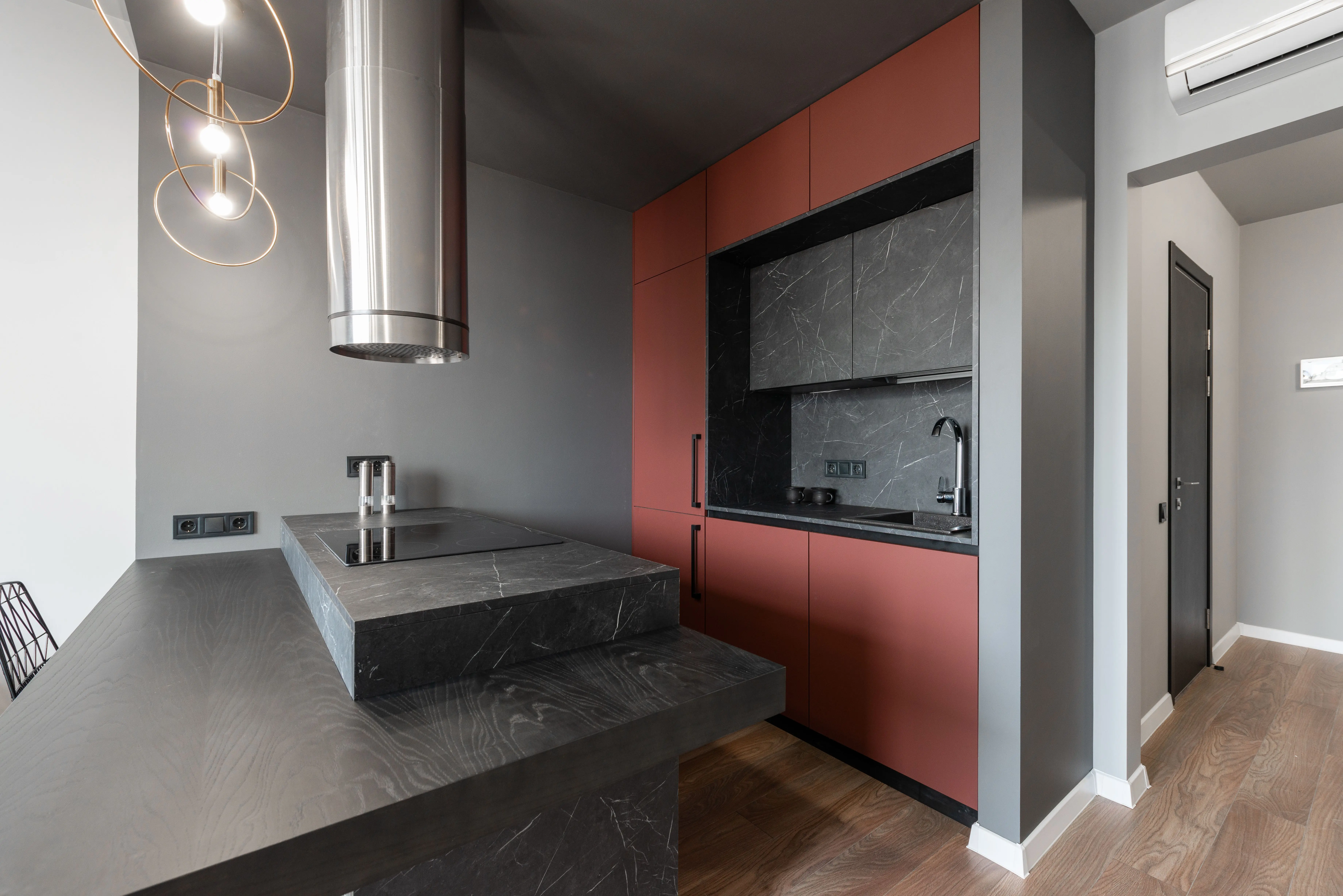 dark gray kitchen cabinets Contemporary minimalist island style kitchen with metal tube range hood over counter with built in stove in modern apartment