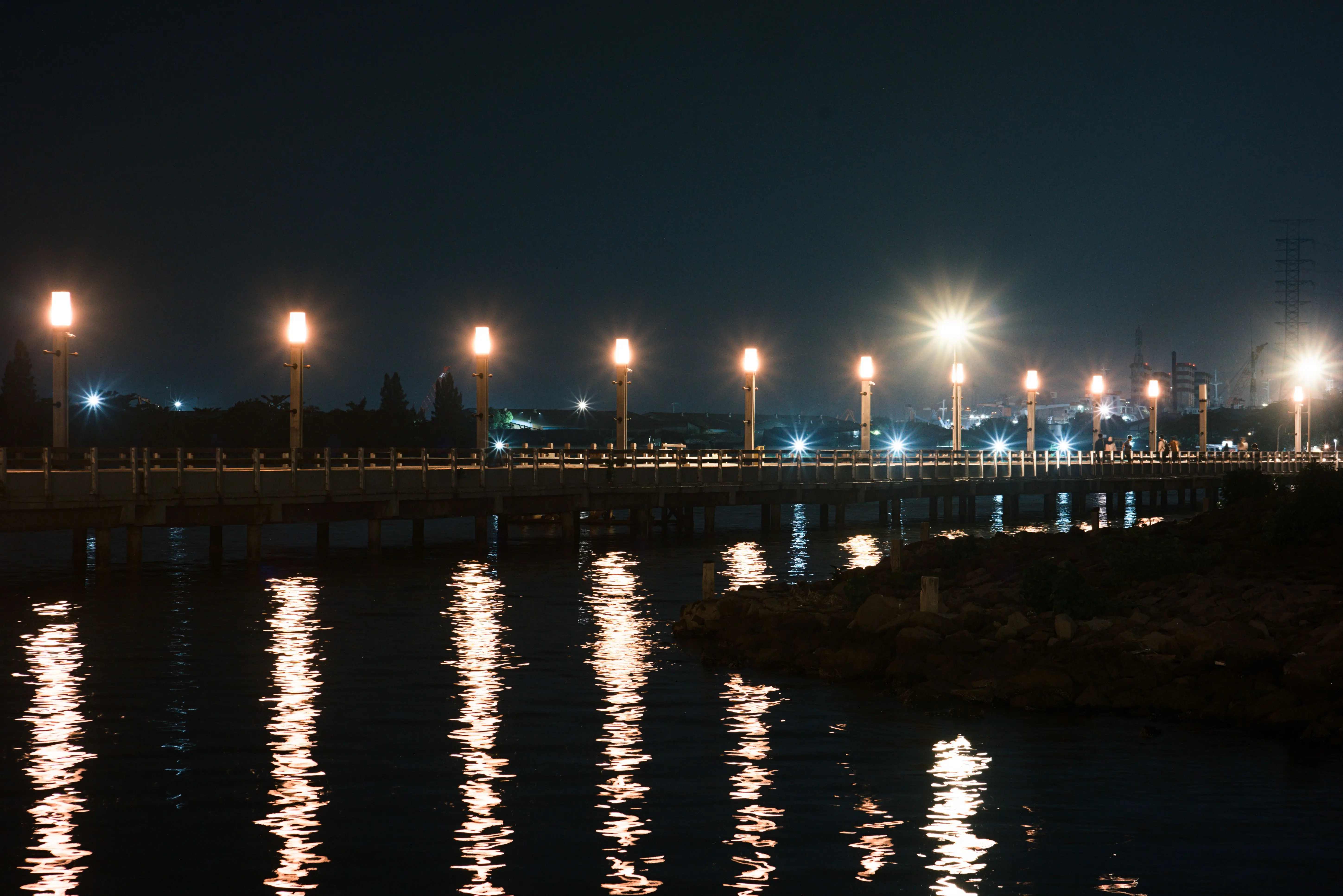 deck post lights Scenic night view of a coastal pier with glowing lights reflecting on the water.
