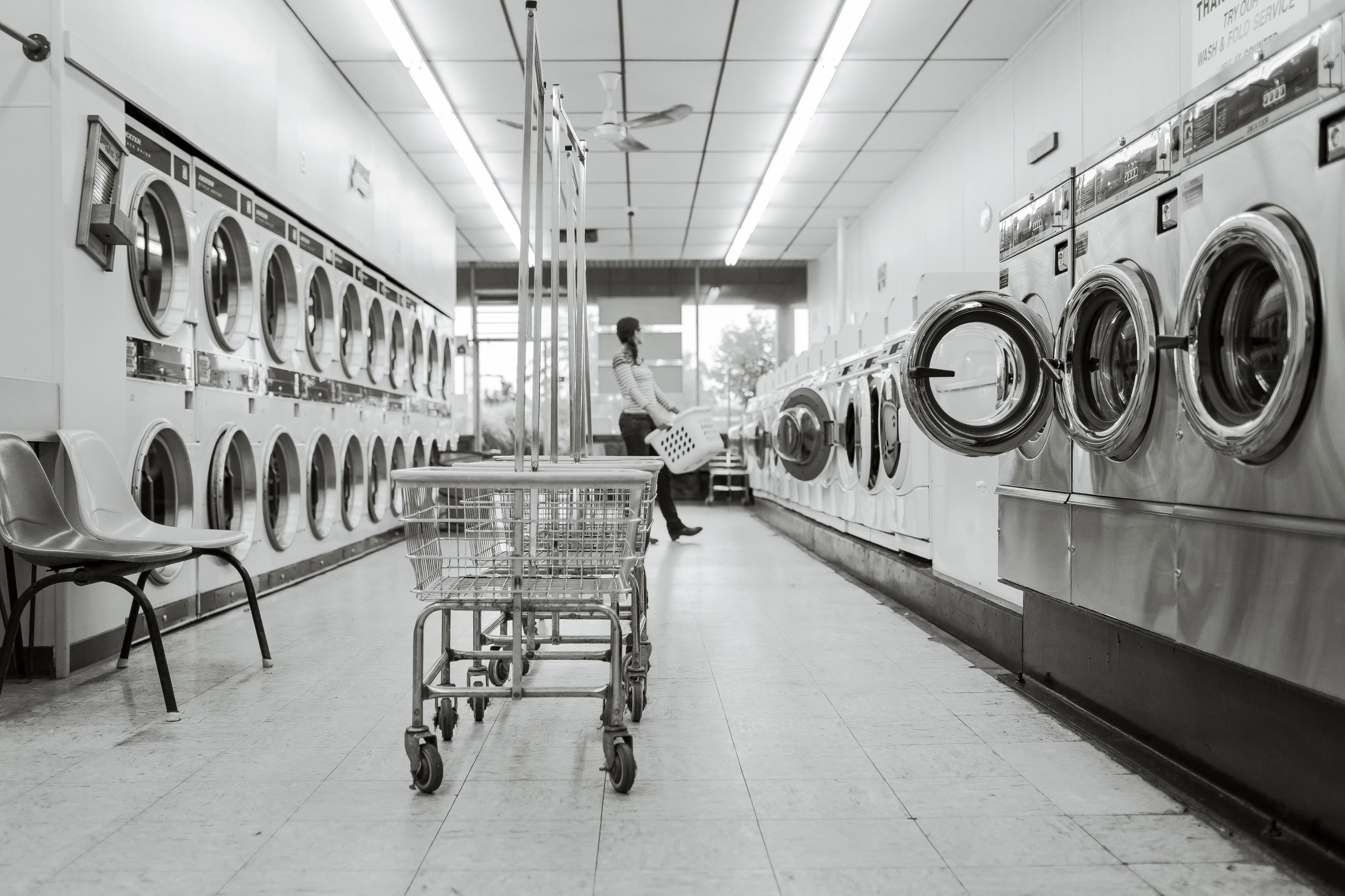 dryer does not heat Black and white image of a laundromat with laundry machines and a person in the background.