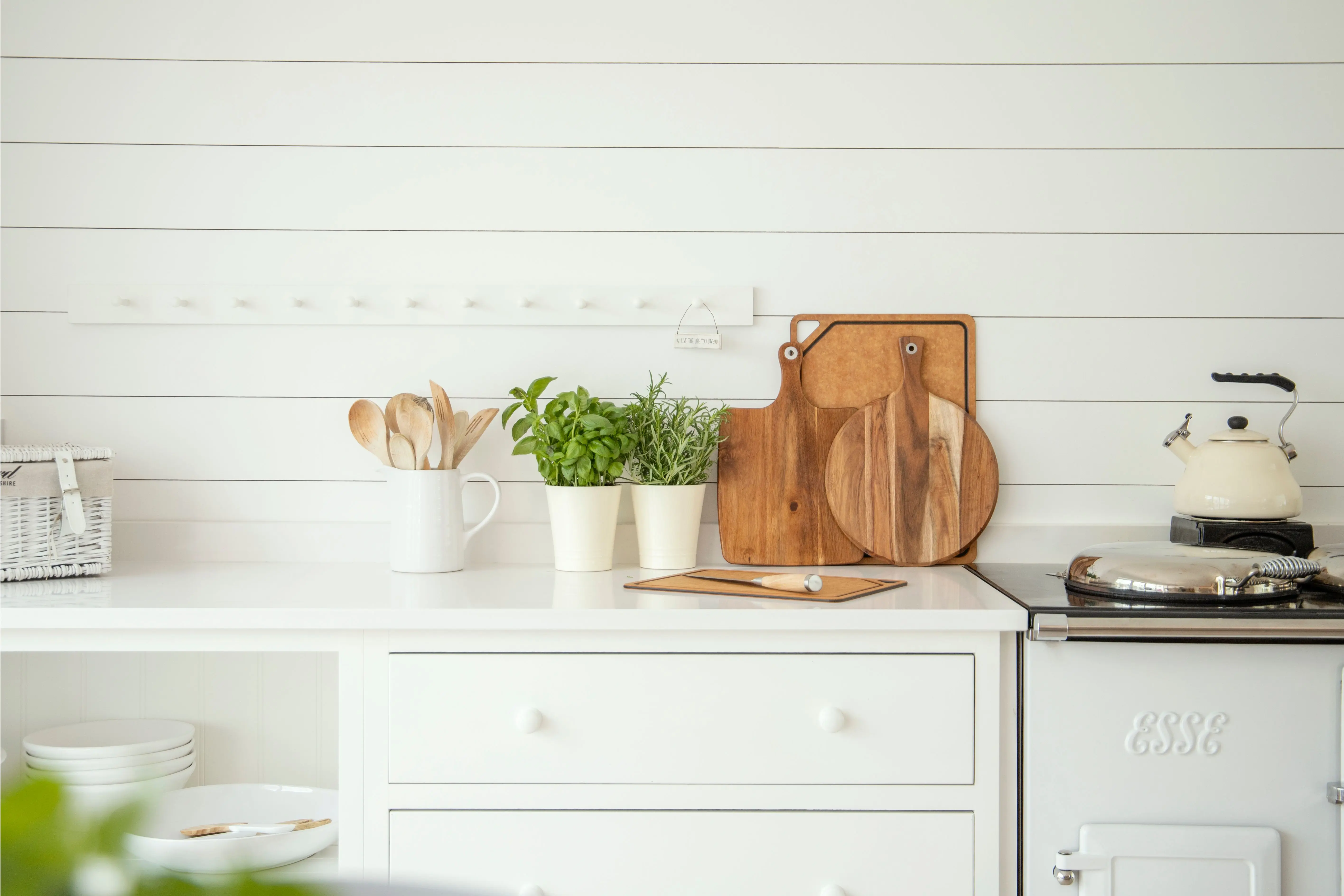 farmhouse kitchen cabinets Stylish kitchen counter with herb pots, cutting boards, and utensils against a white backdrop.
