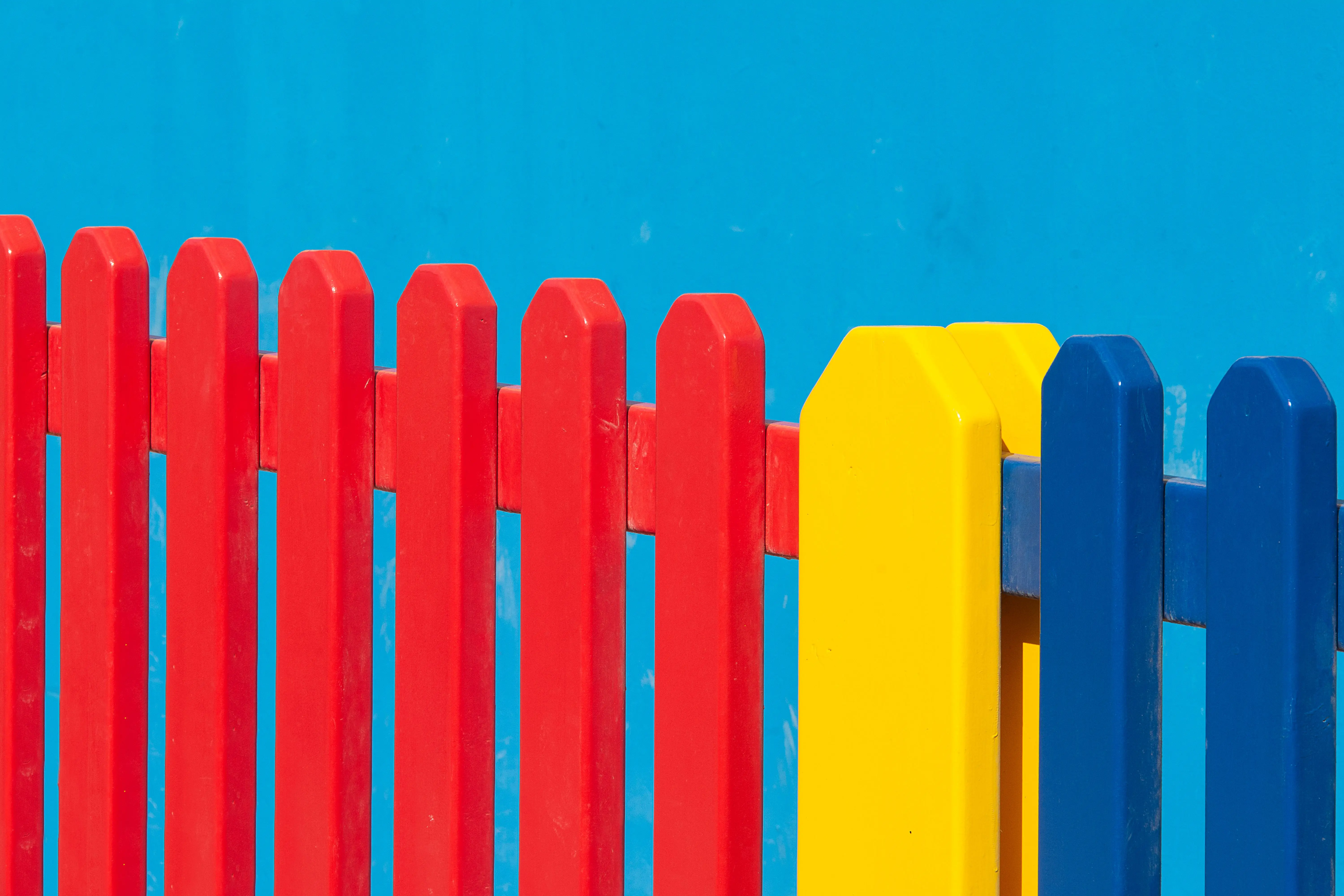 fence cost Vibrant red, yellow, and blue wooden fence panels against a clear blue backdrop.