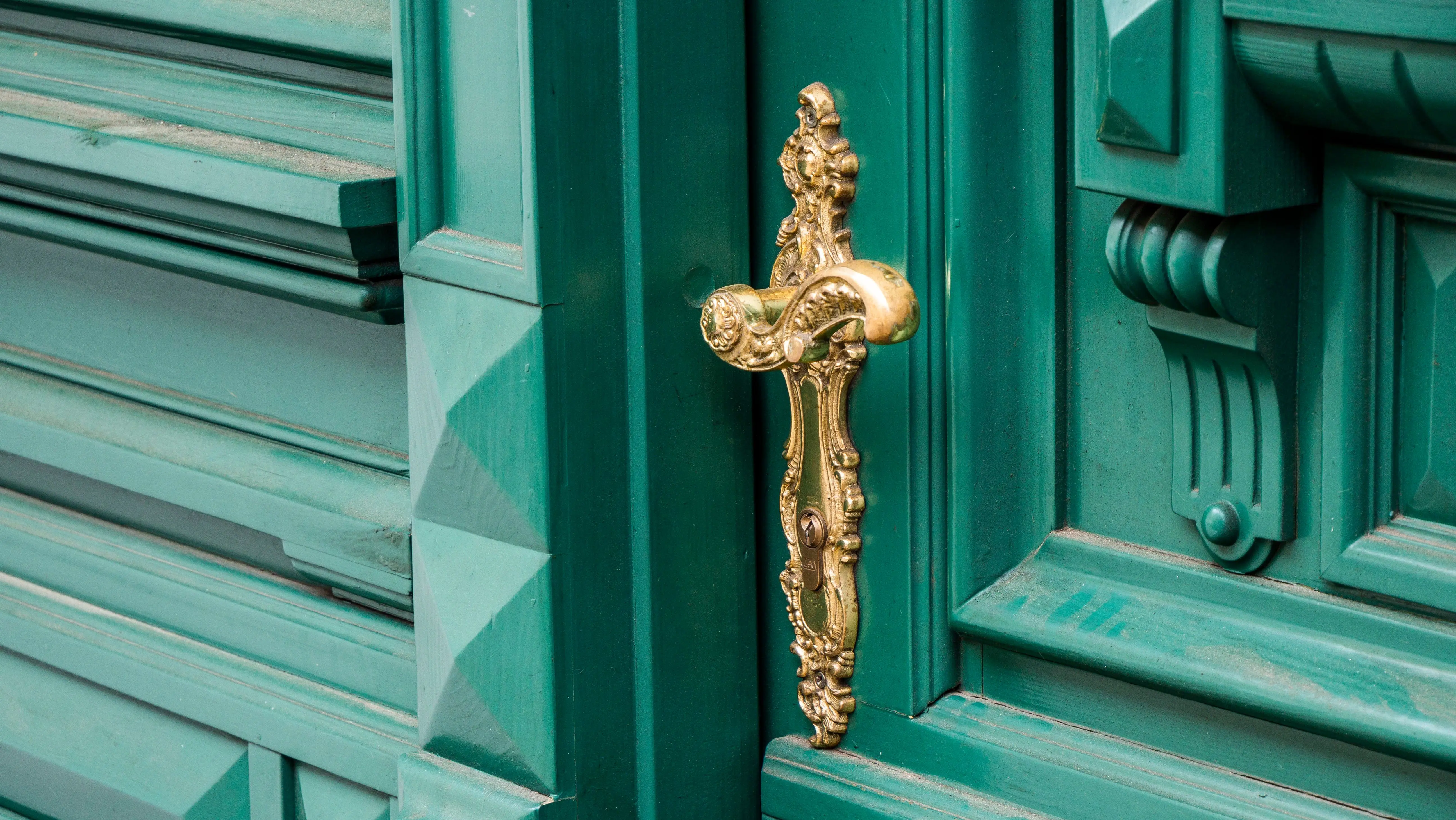 gold drawer pulls Close-up of an ornate brass door handle on a detailed turquoise wooden door.
