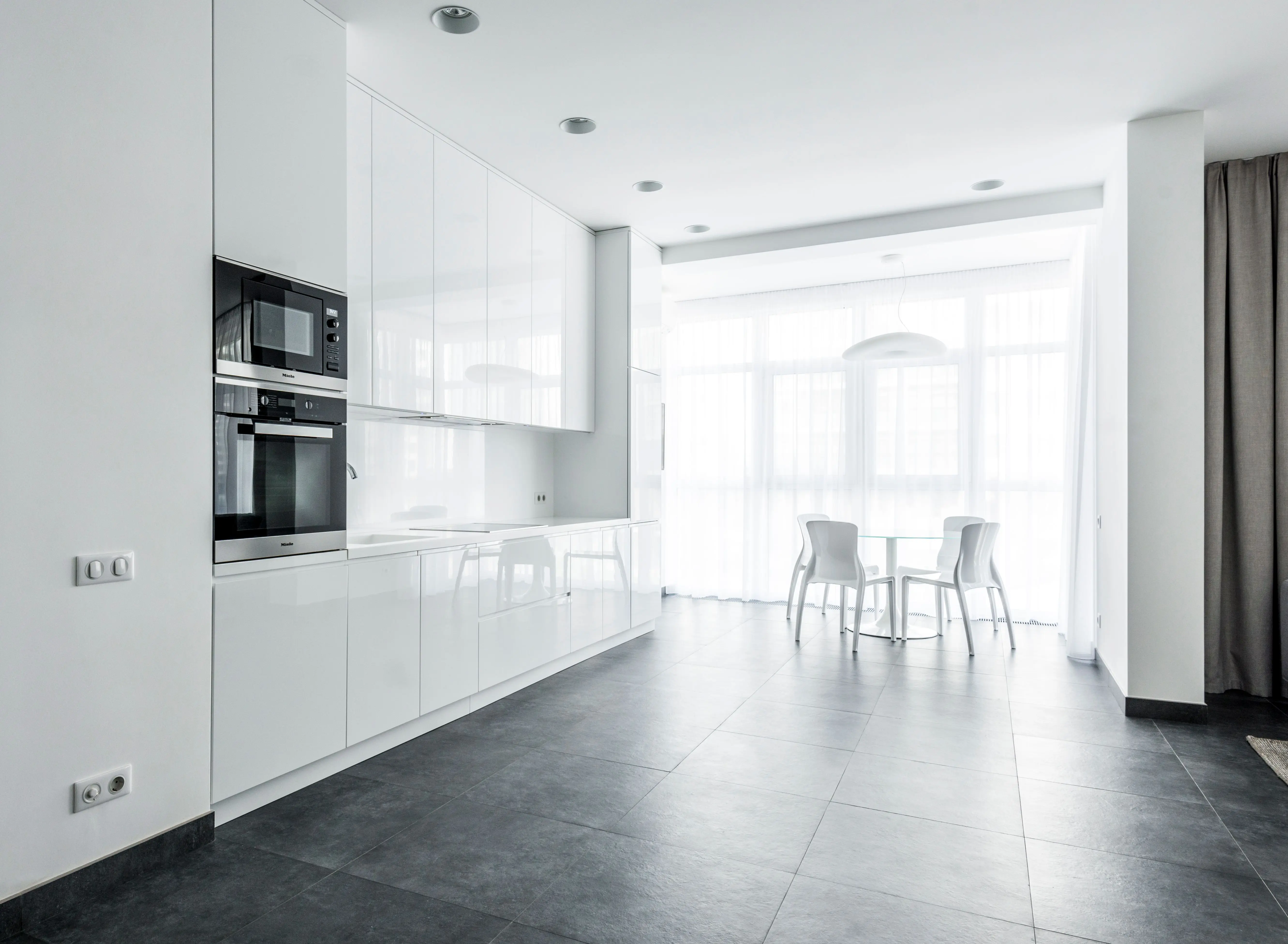 black cabinet knobs Bright minimalist kitchen featuring sleek white cabinetry and dining space.