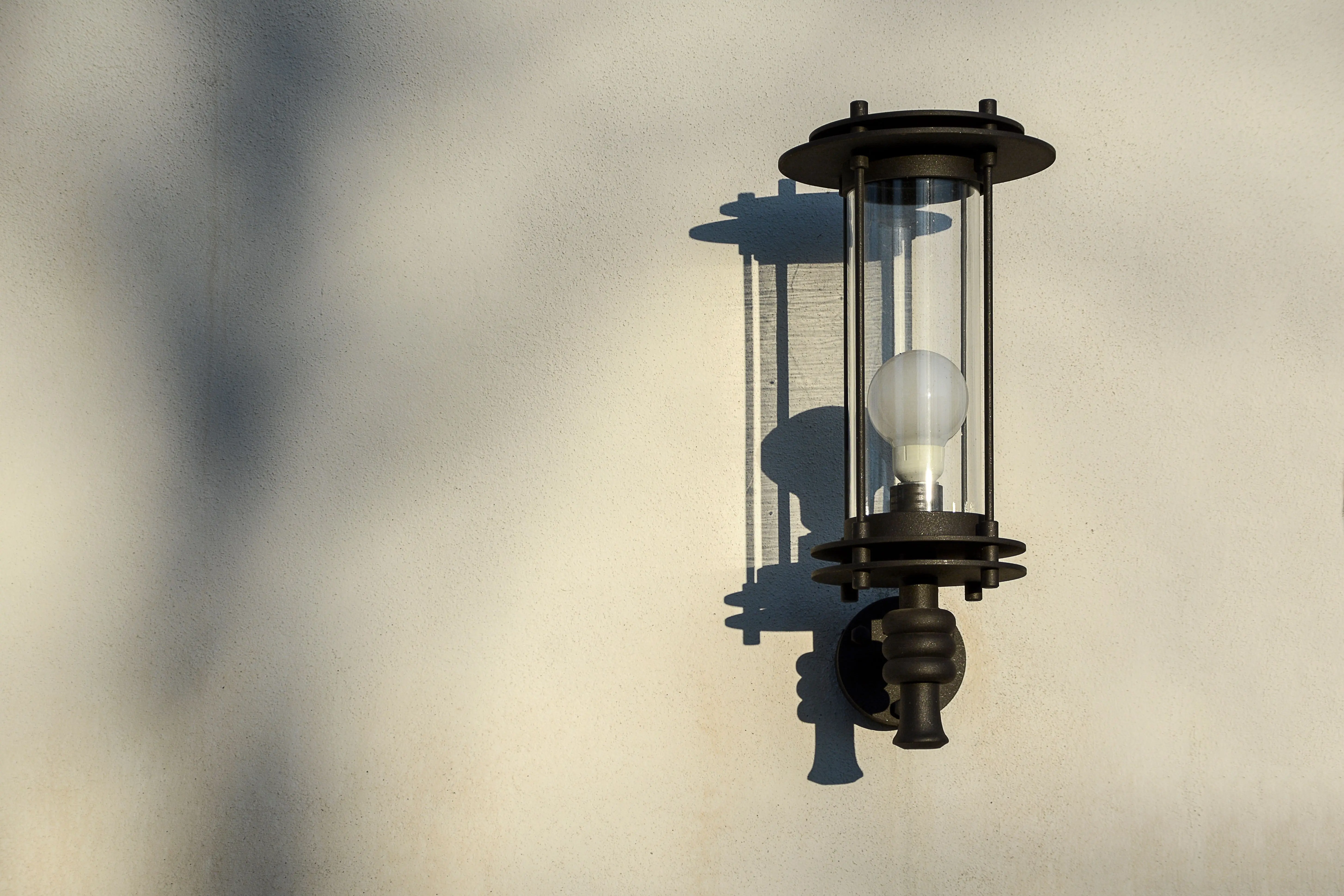 wall lamp outdoor Elegant outdoor wall light casting shadow on textured wall in sunlight.