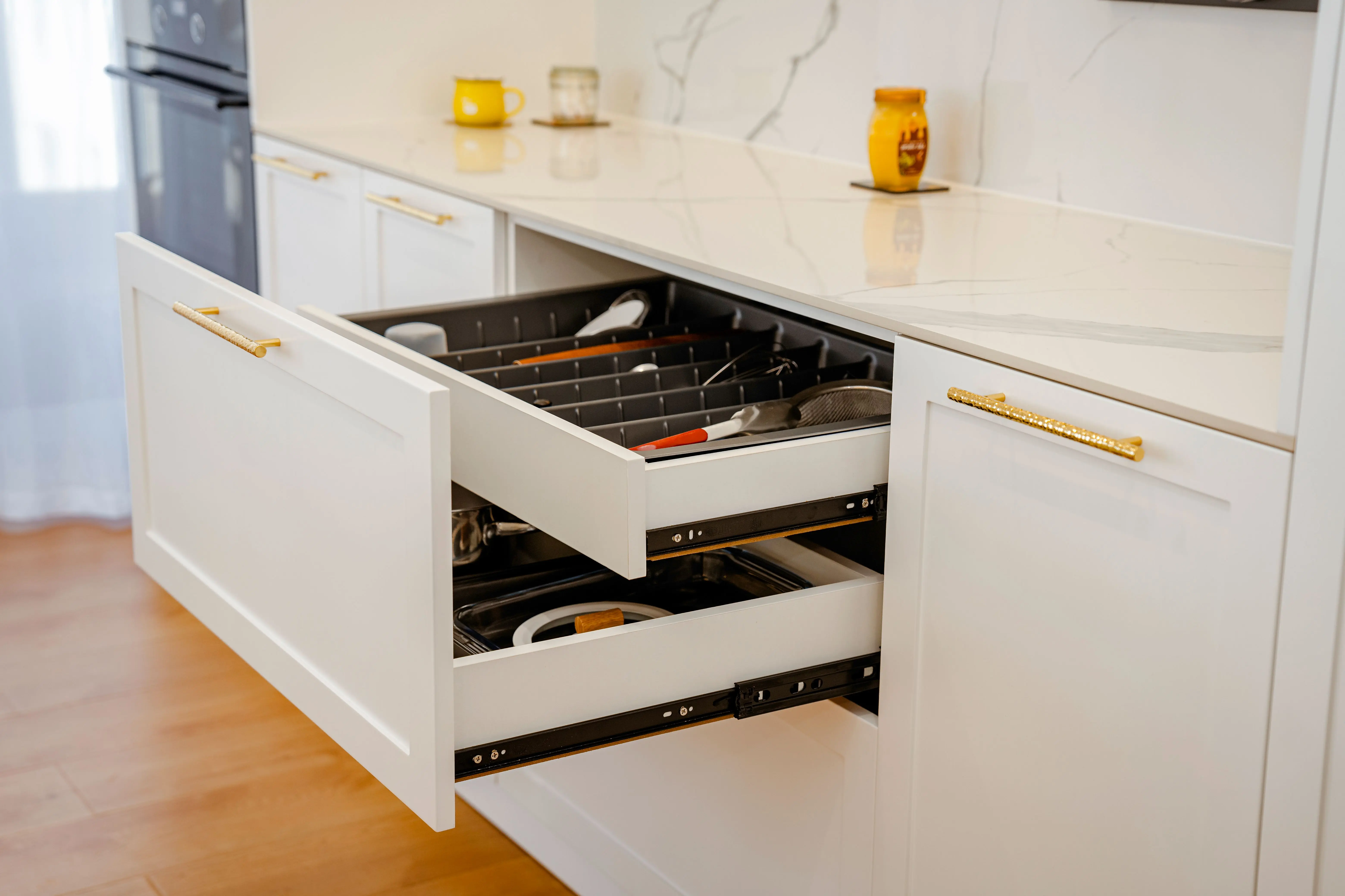 gold drawer pulls Elegant white kitchen drawer open with utensils, on marble counter.