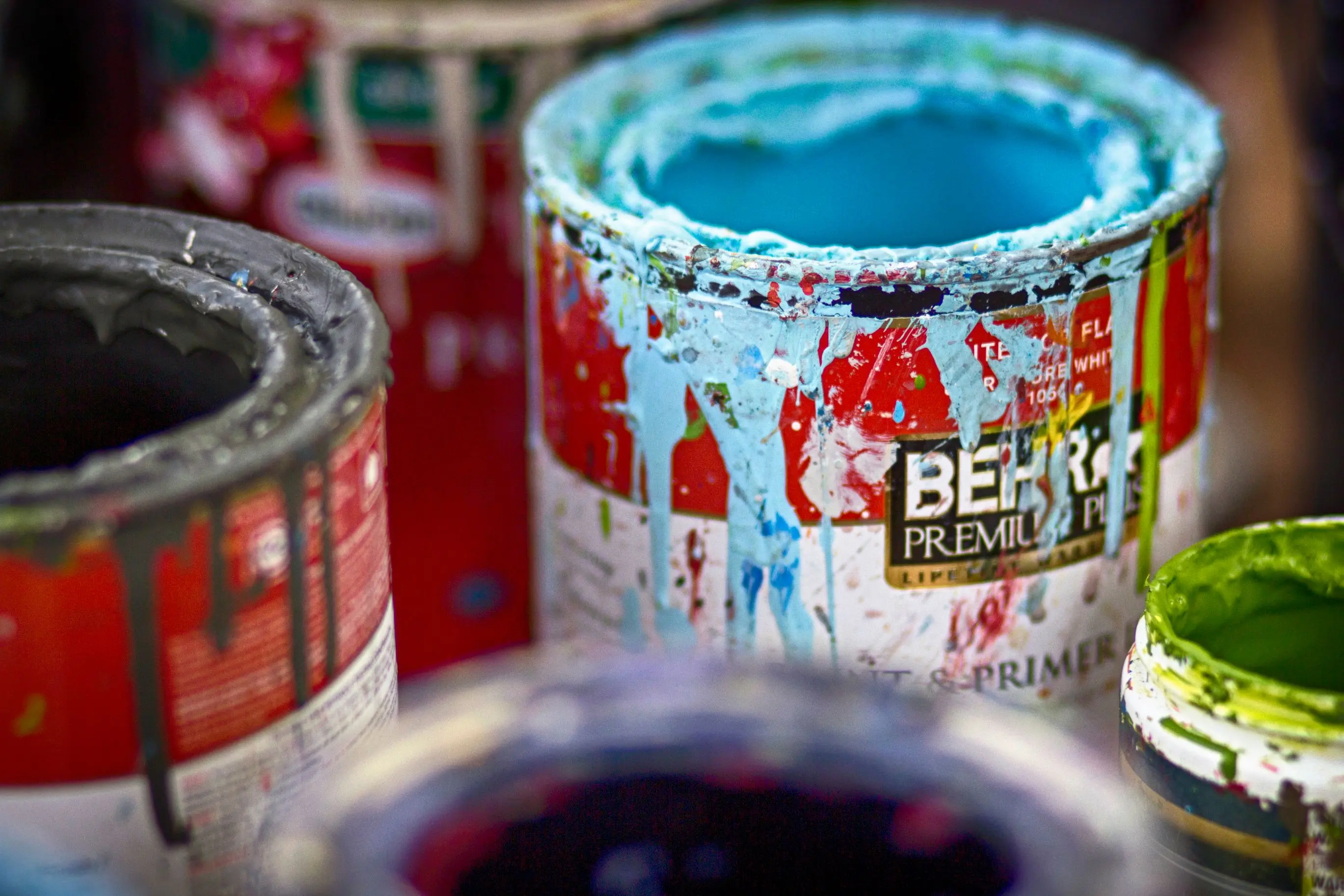 a water based paint Close-up of vibrant, messy open paint cans with colorful splatters on a workshop surface.