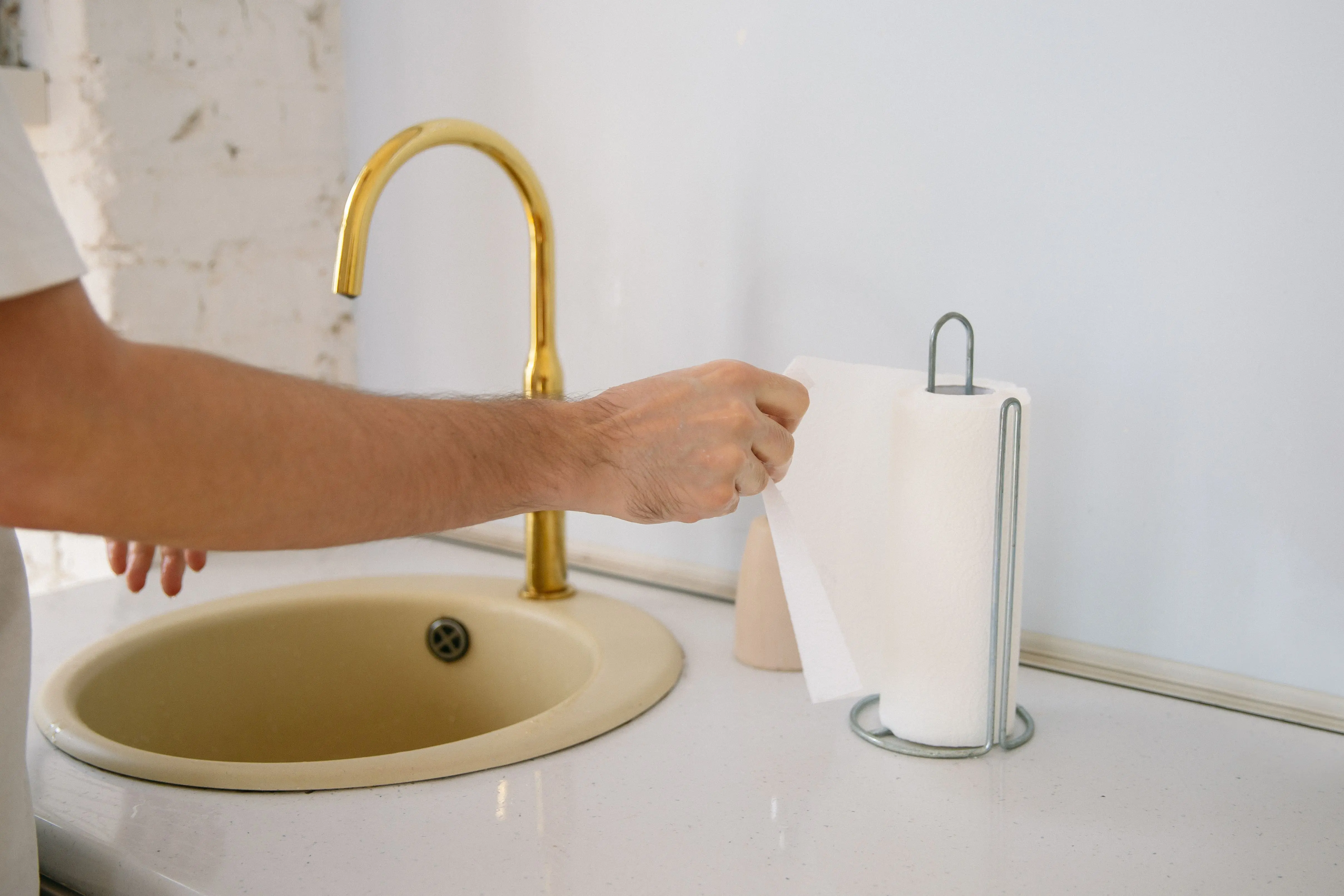 and paper towels A bathroom sink with a golden faucet and hand reaching for a paper towel in a clean setting.