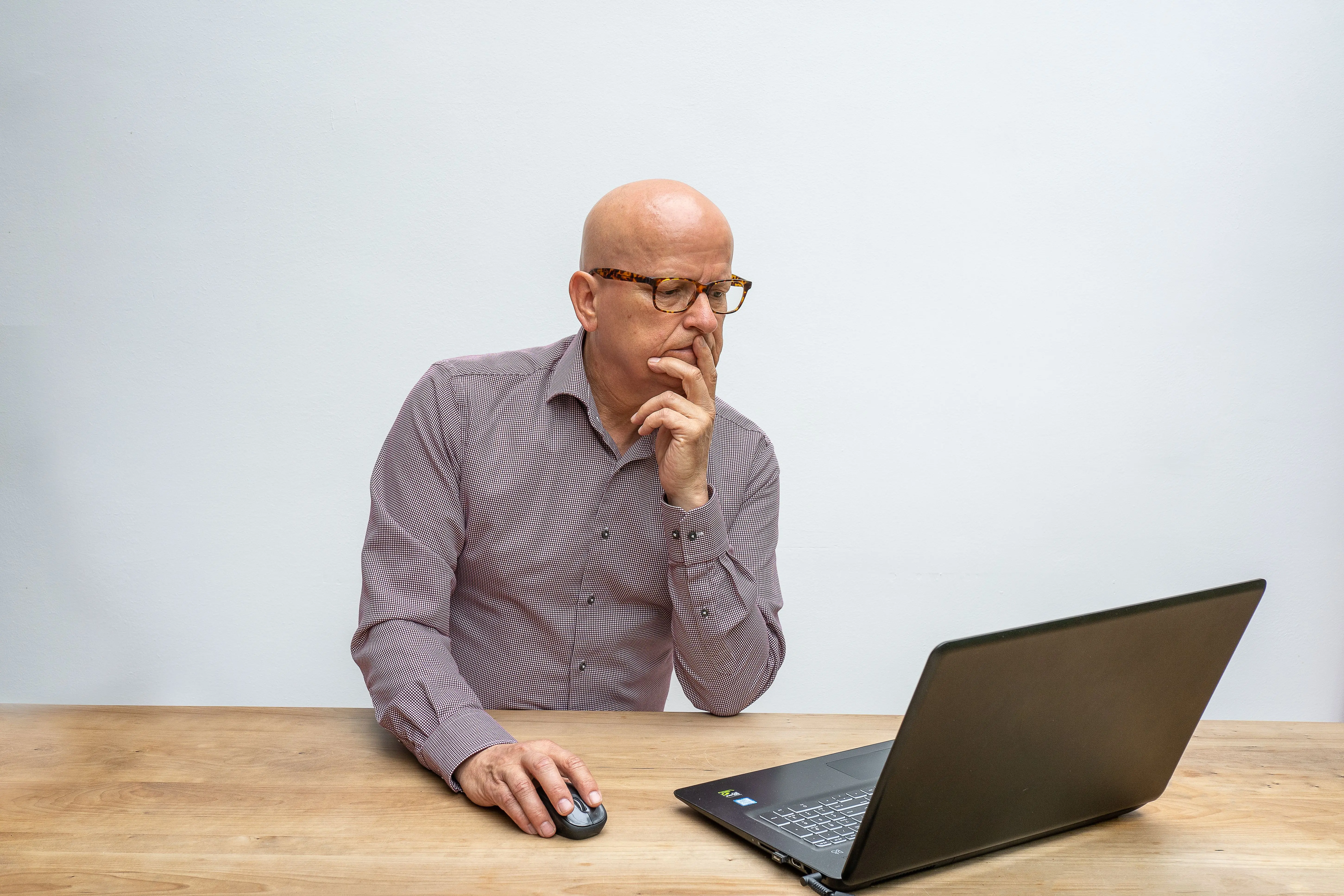 do mice bite Bald elderly man with glasses using a laptop and mouse at a wooden table.