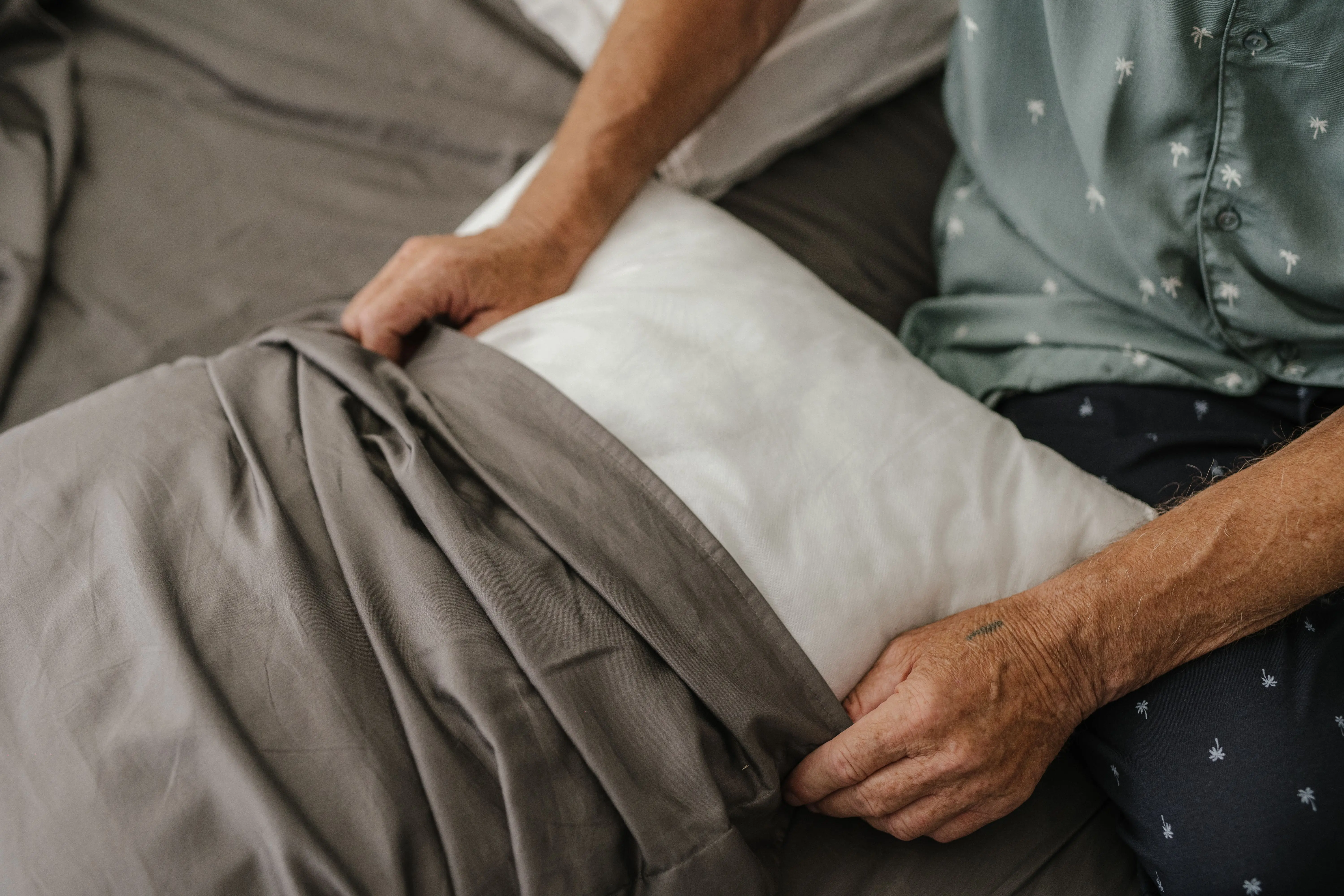 blue decorative pillows Close-up of a senior adult carefully arranging a bed with grey sheets and a white pillow.