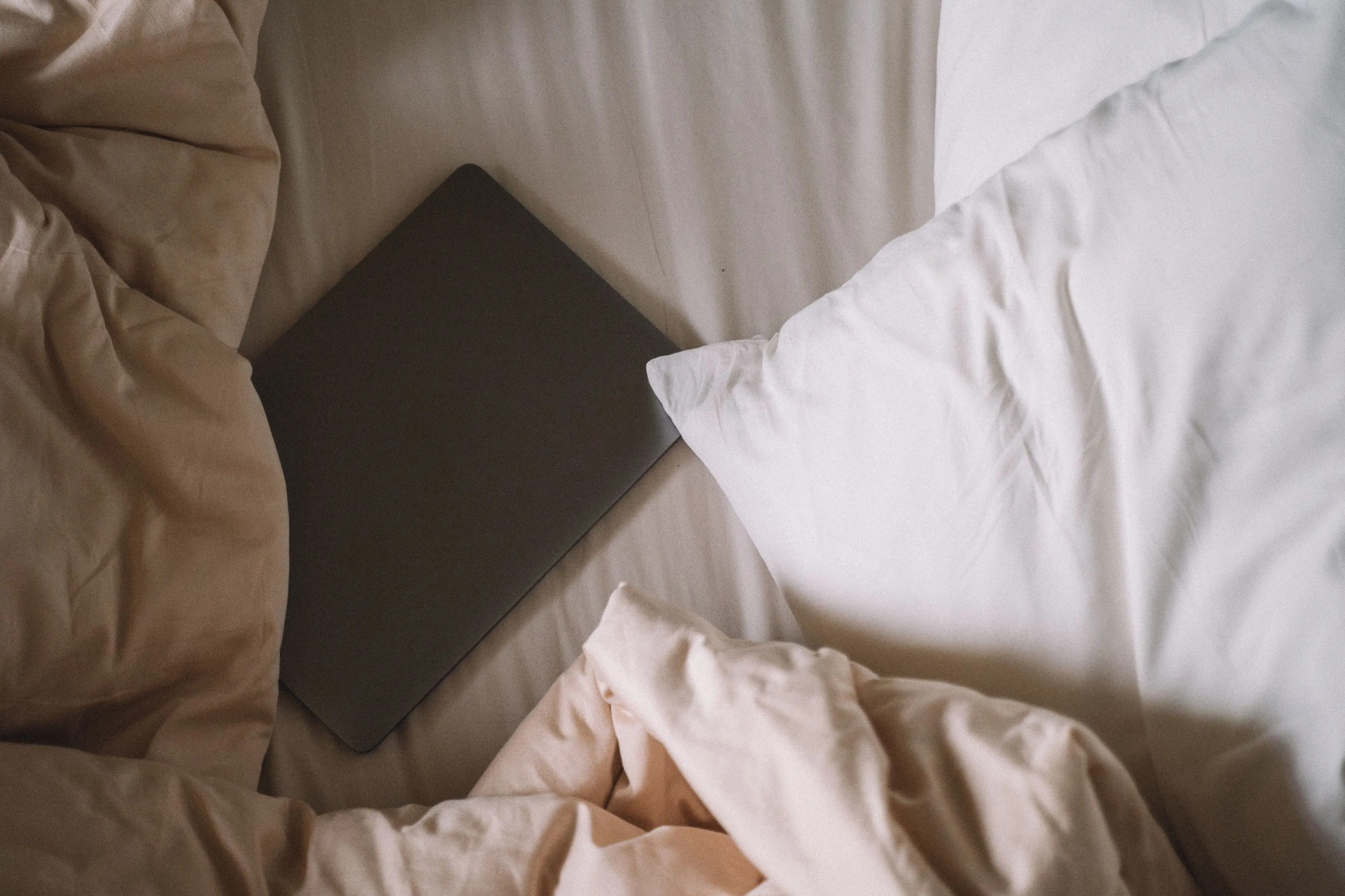 blue decorative pillows A laptop resting on an unmade bed with soft linens, offering a cozy and relaxed atmosphere.