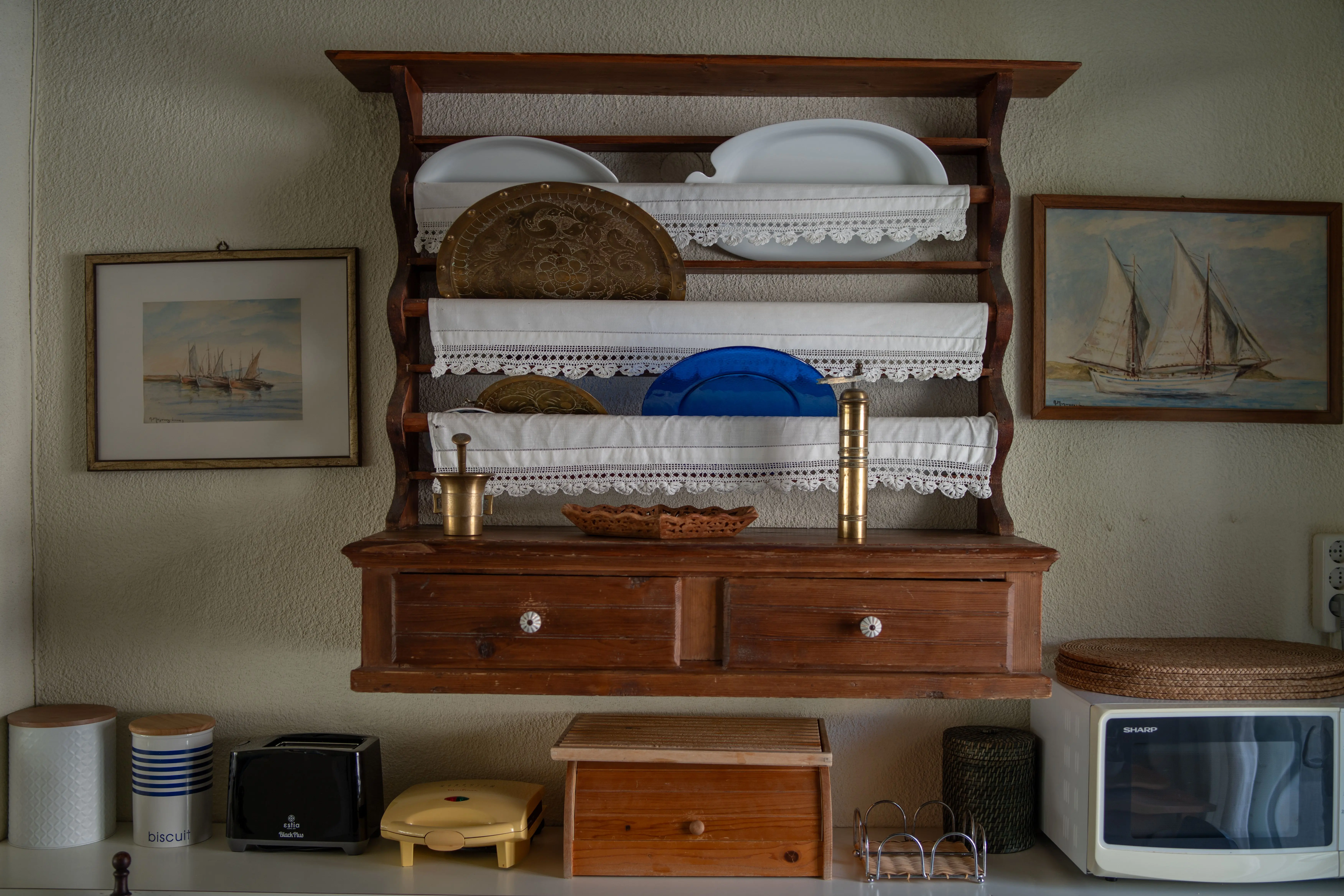 plate racks Vintage kitchen with wooden shelves displaying plates and nautical-themed paintings.
