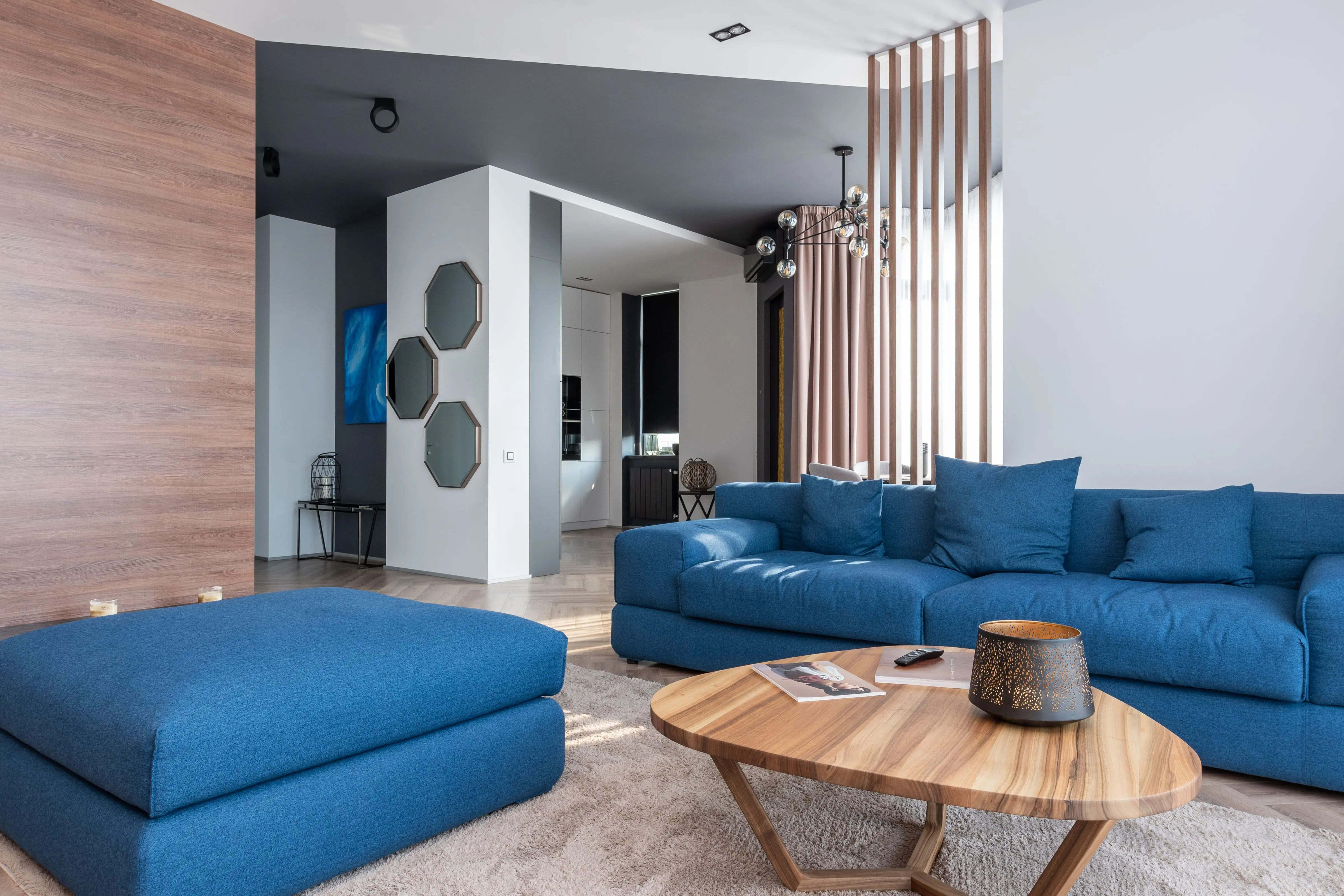 pouf coffee table Interior of contemporary flat with blue couch and pouf placed near table in living room near kitchen zone with decorations on wall