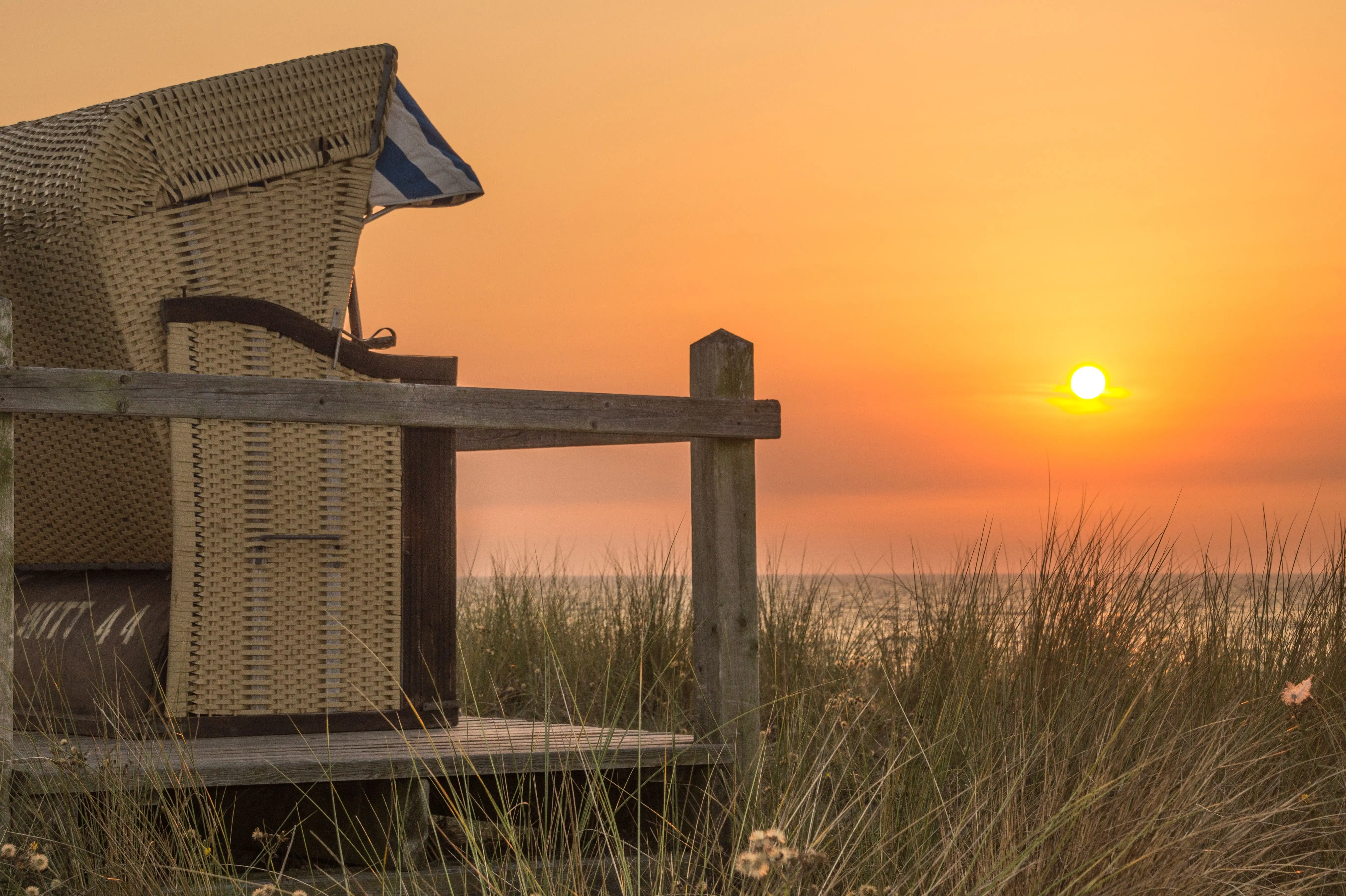 wood outdoor chairs Serene beach view with wicker chair at sunset, capturing the beauty of nature and tranquility.