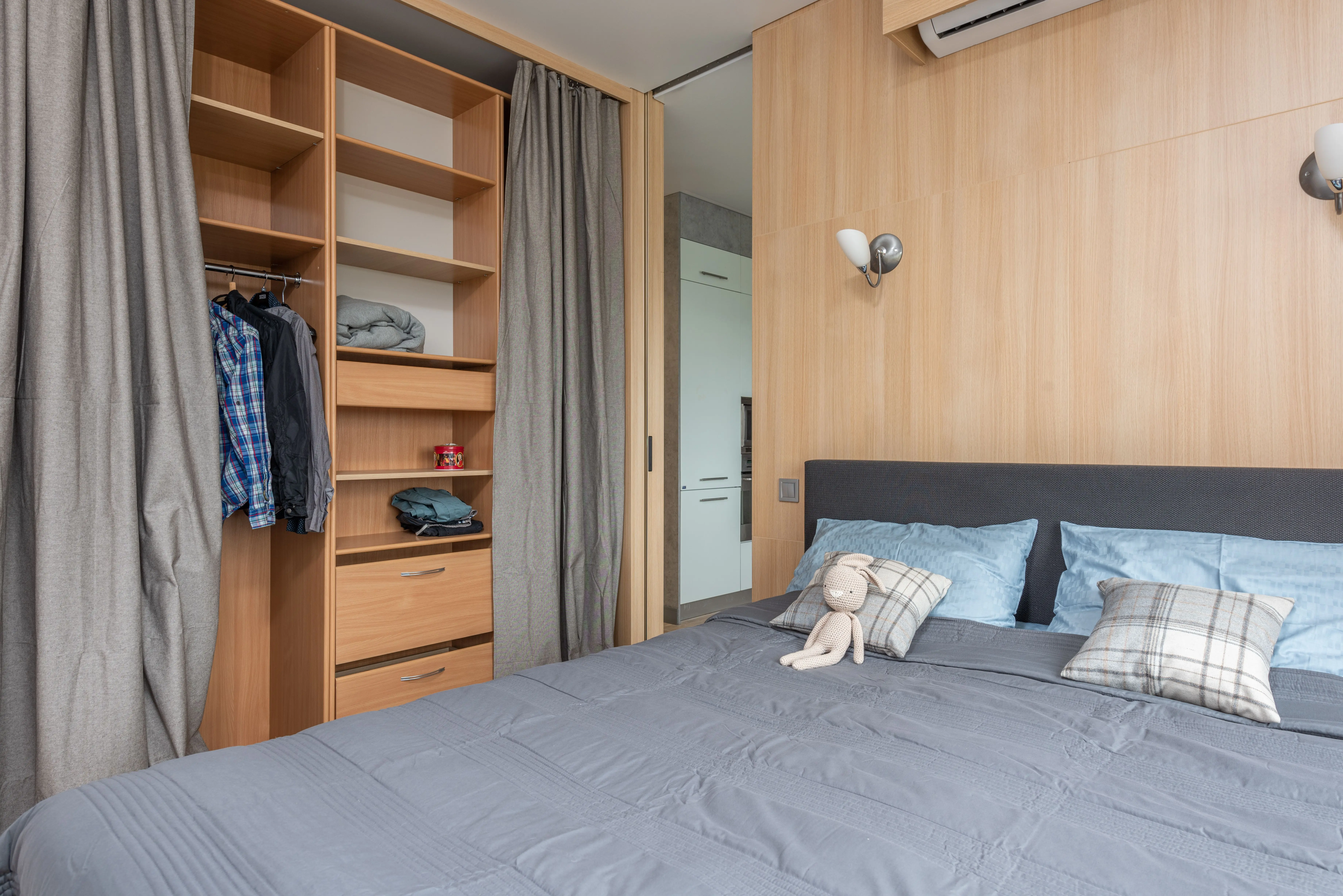 twin platform bed with storage Modern room interior with bed with pillows and soft rabbit toy near wooden wardrobe with curtains and shelves near clothes on hangers and entrance to kitchen in bright flat