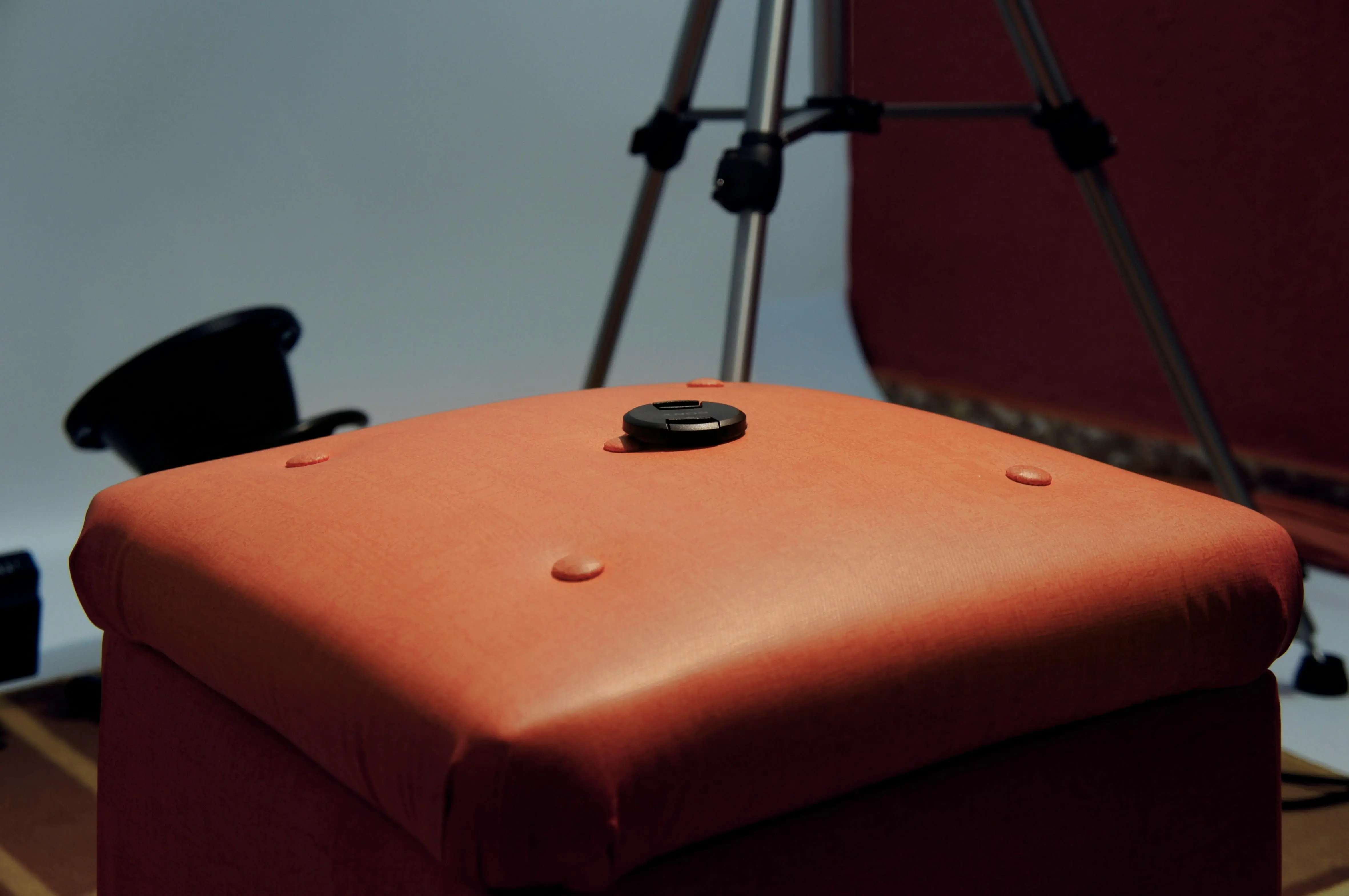 studio room ideas Focus on brown ottoman with camera lens cap in indoor studio setup, no people visible.