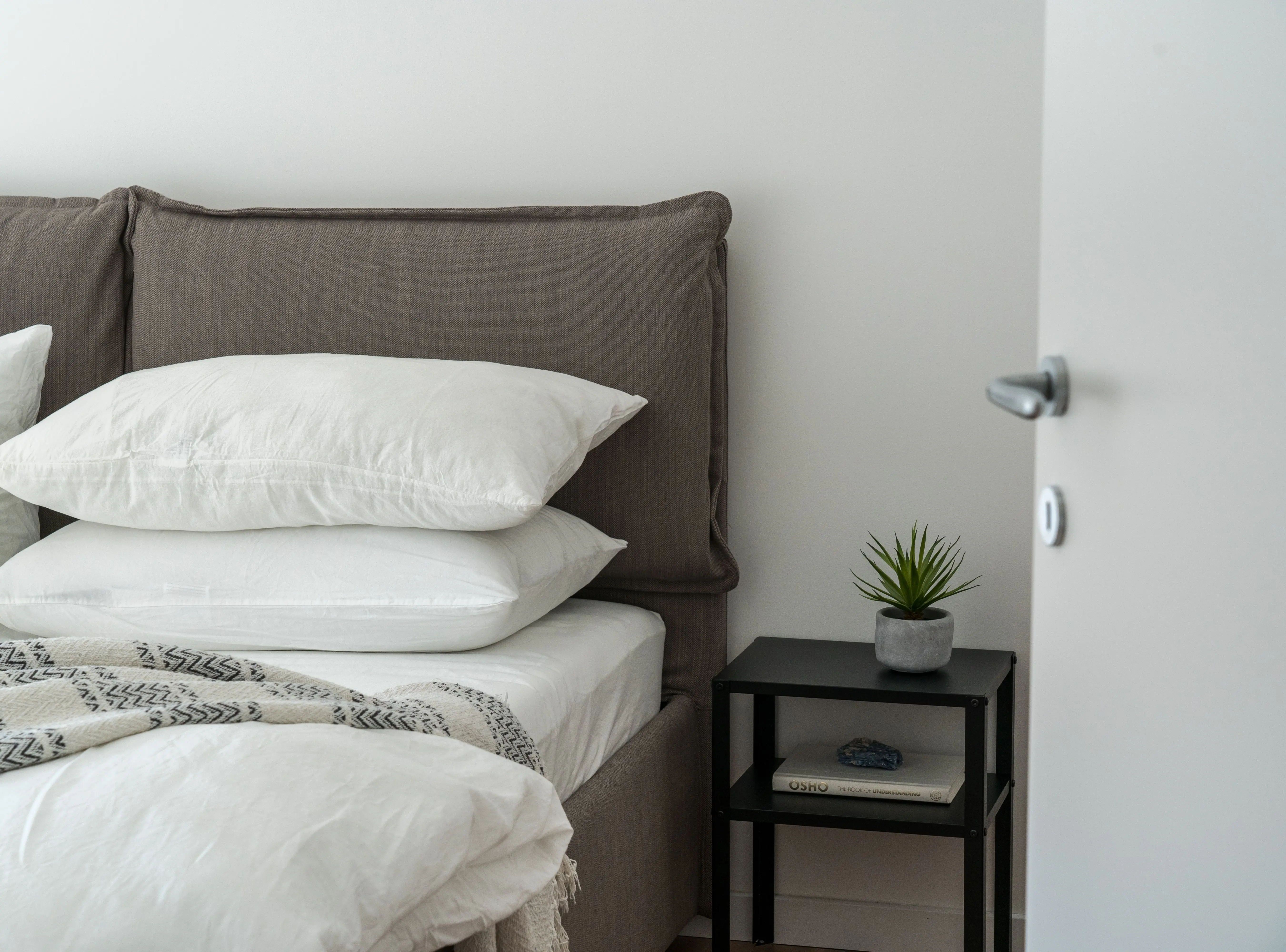 white pillow A serene and stylish bedroom featuring a comfortable bed with clean white bedding and a side table with decor.