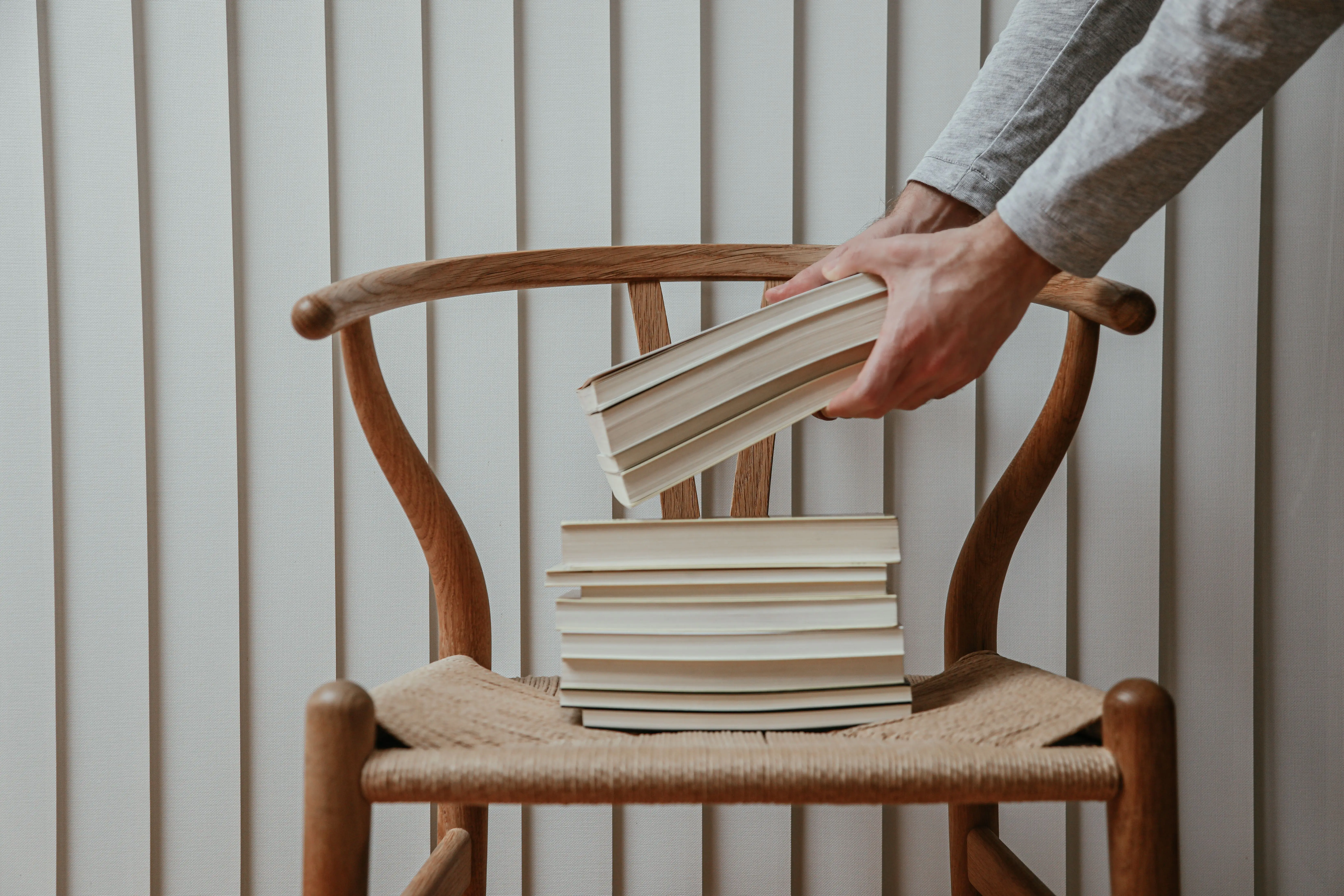 wood outdoor chairs A person stacks books on a wooden chair against a white wall.