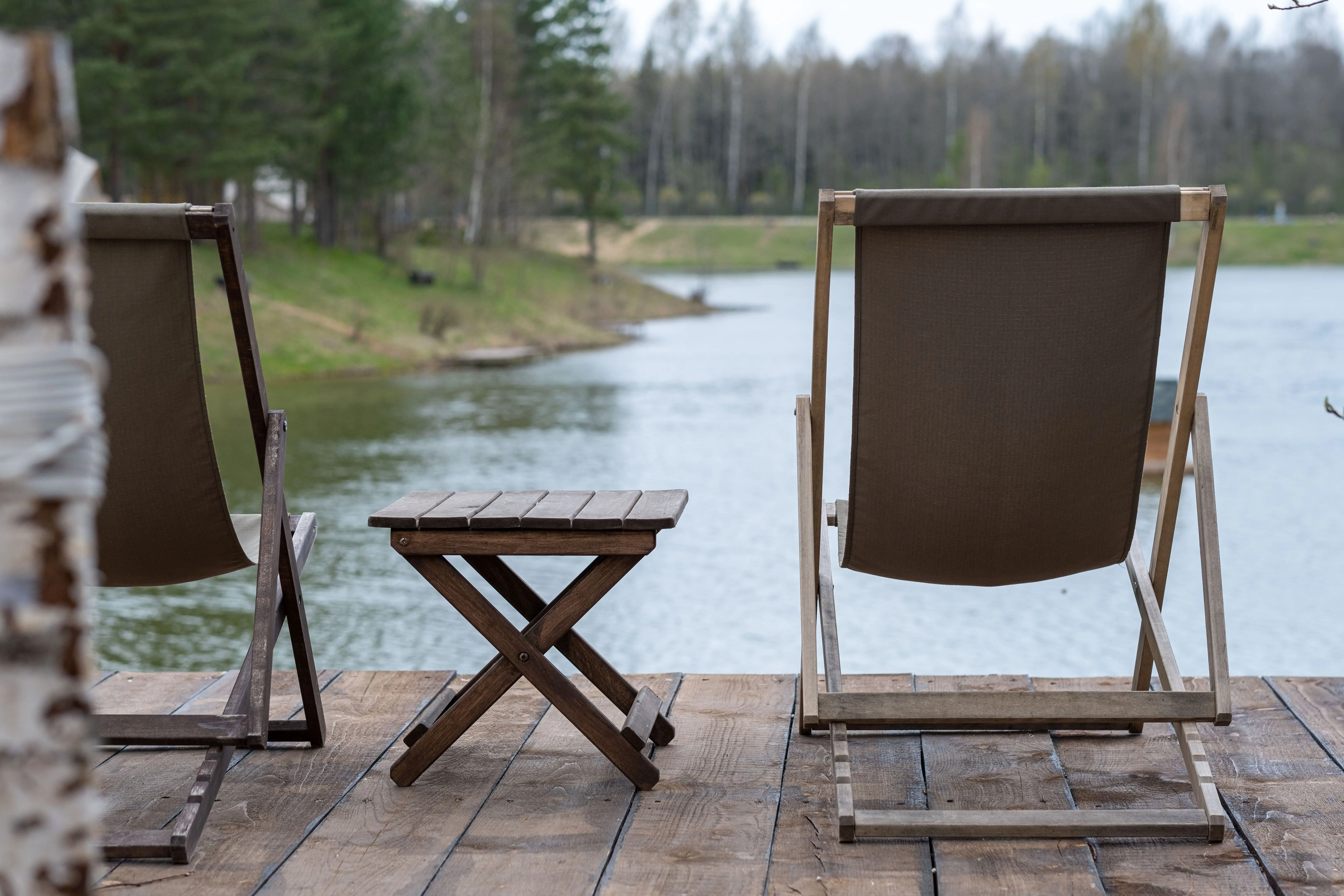 wood outdoor chairs Rustic wooden deck chairs and table overlooking a serene lake and landscape.