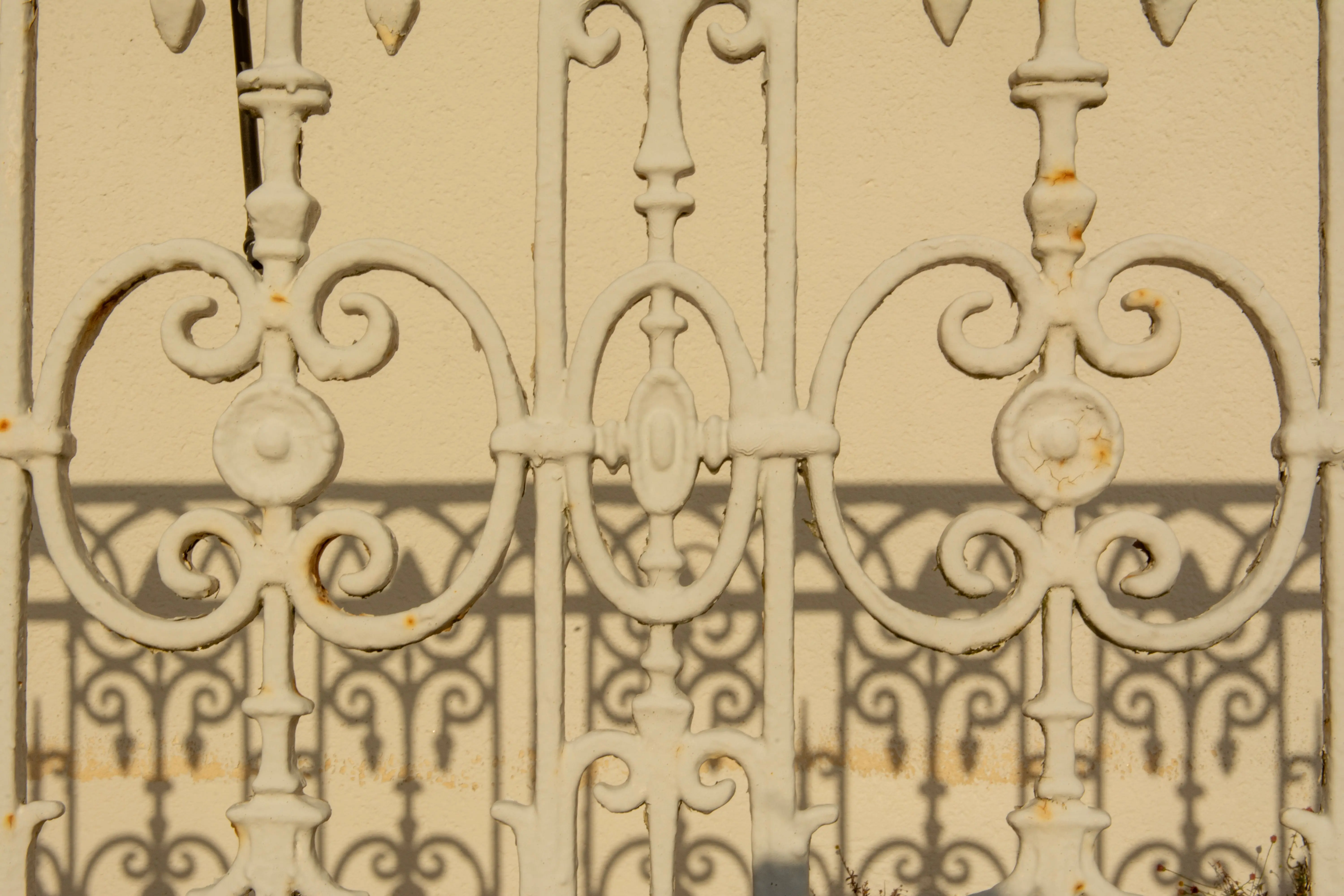 wrought iron patio furniture sets Close-up of an ornate iron fence casting detailed shadows on a wall.