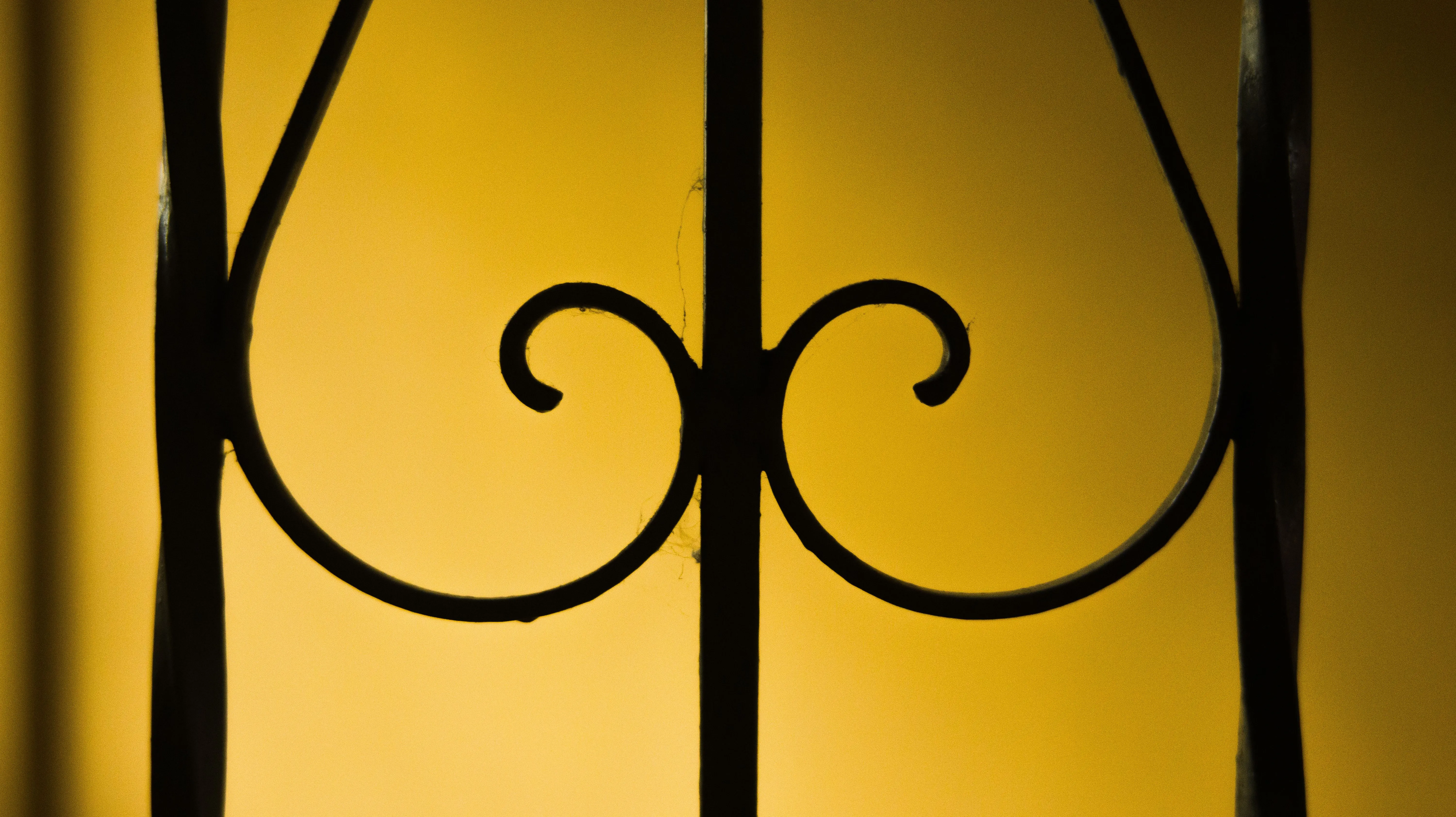 wrought iron patio furniture sets Closeup part of metal fence with ornamental details on background of yellow wall with shadow