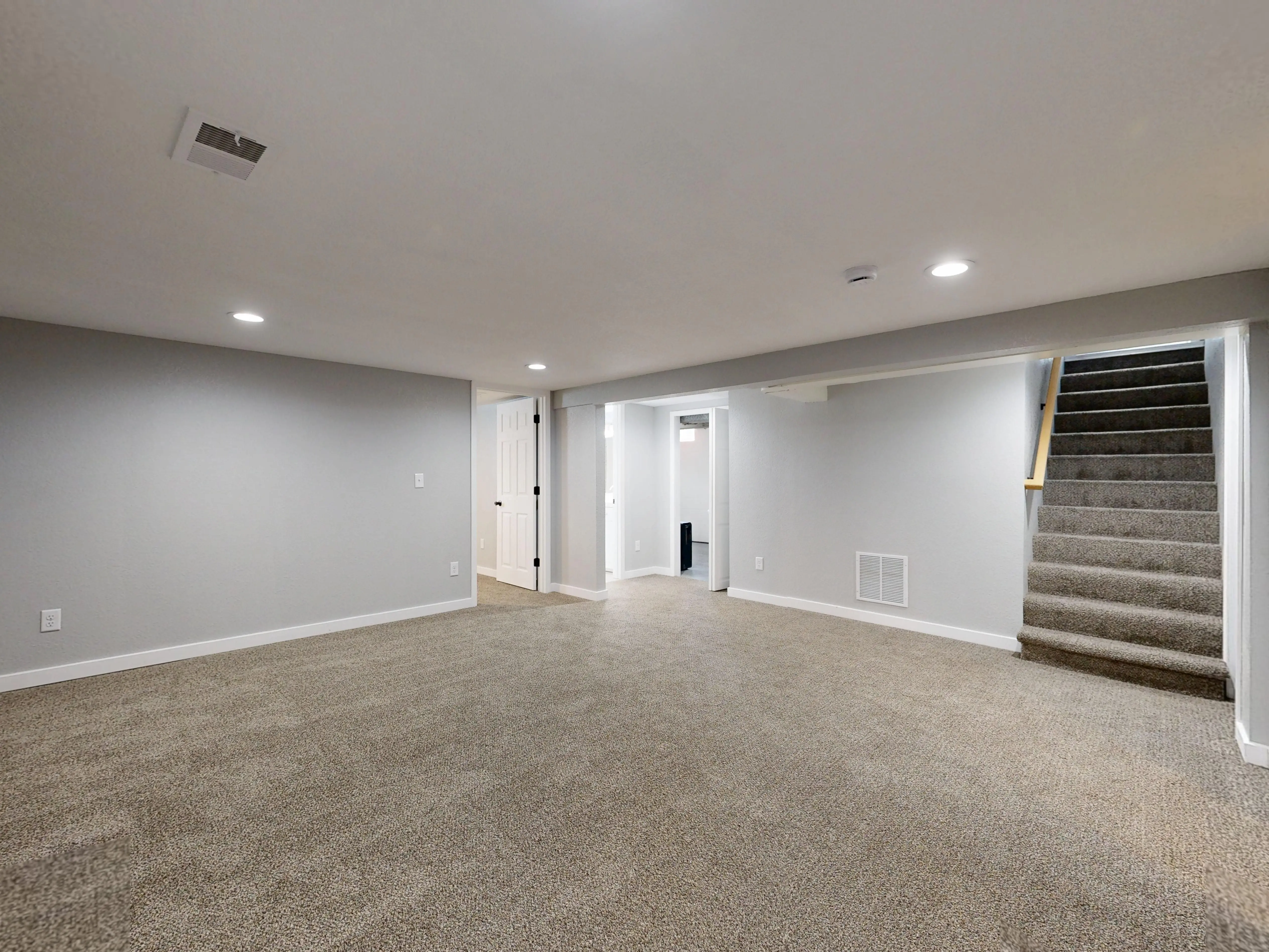 basement remodel cost Empty modern basement with beige carpet and white walls, ideal for renovation.