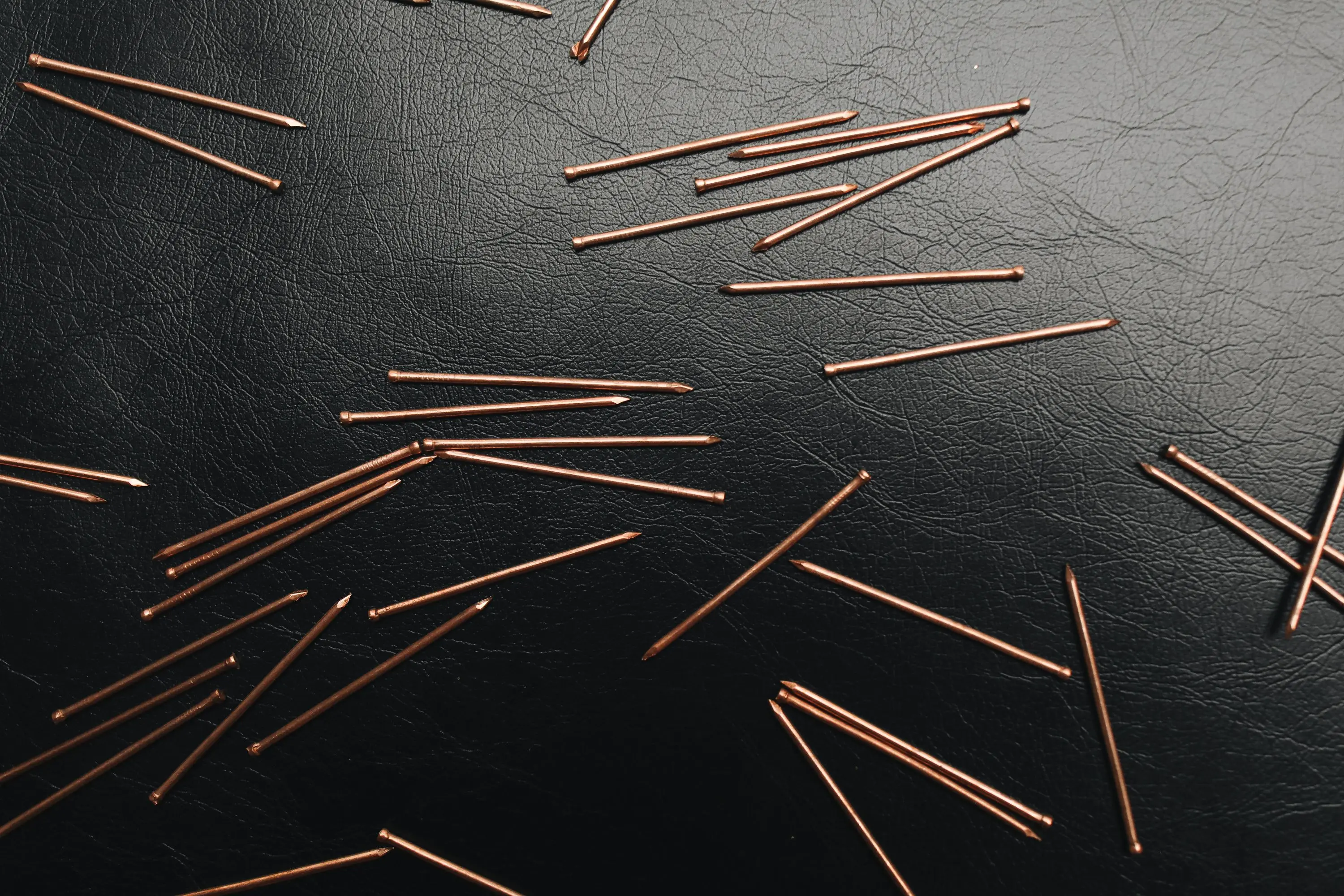 metal desk legs Close-up of copper pins scattered on a textured black leather background.