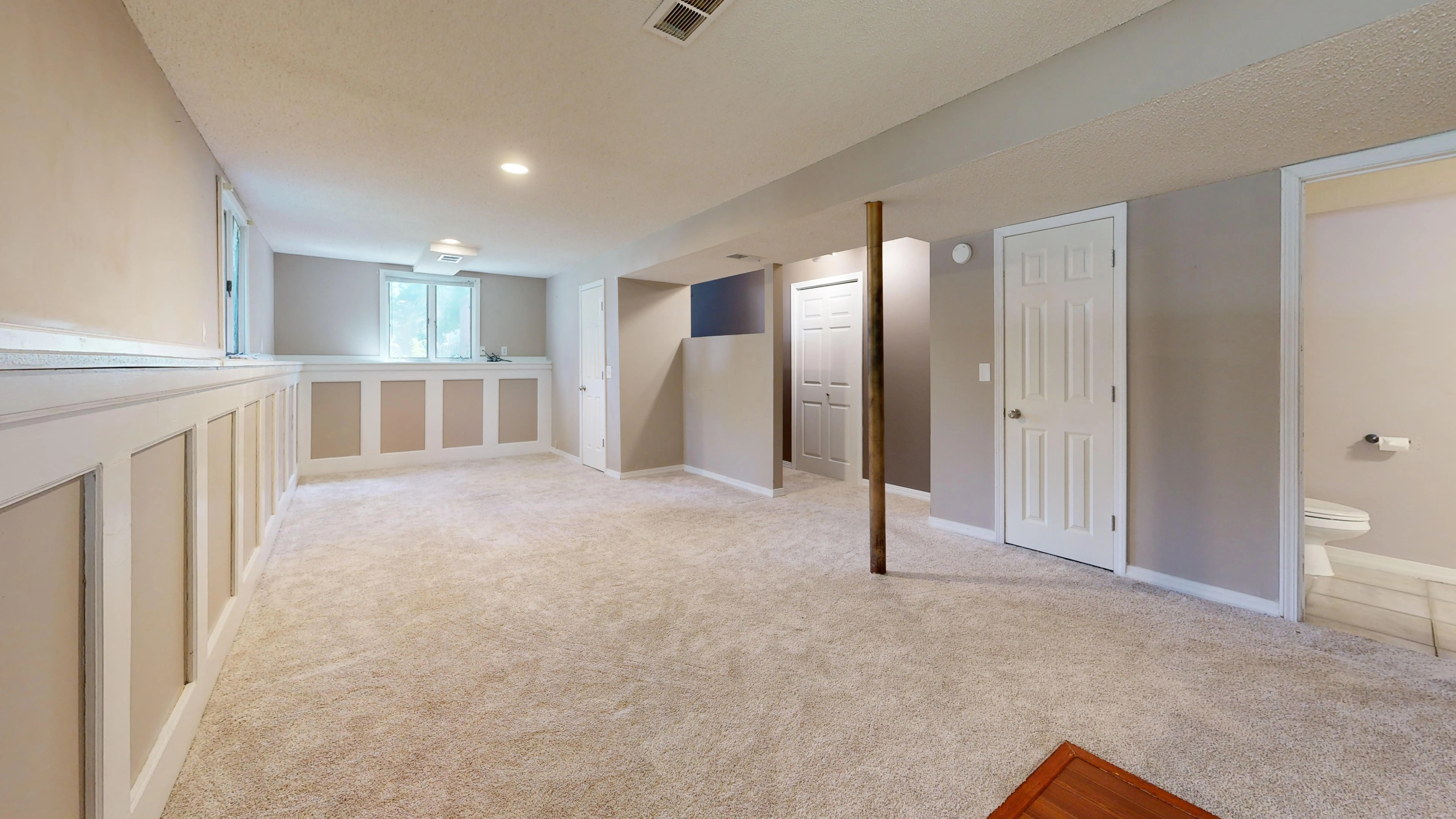 basement remodel cost Bright and clean modern basement with carpet flooring and recessed lighting.