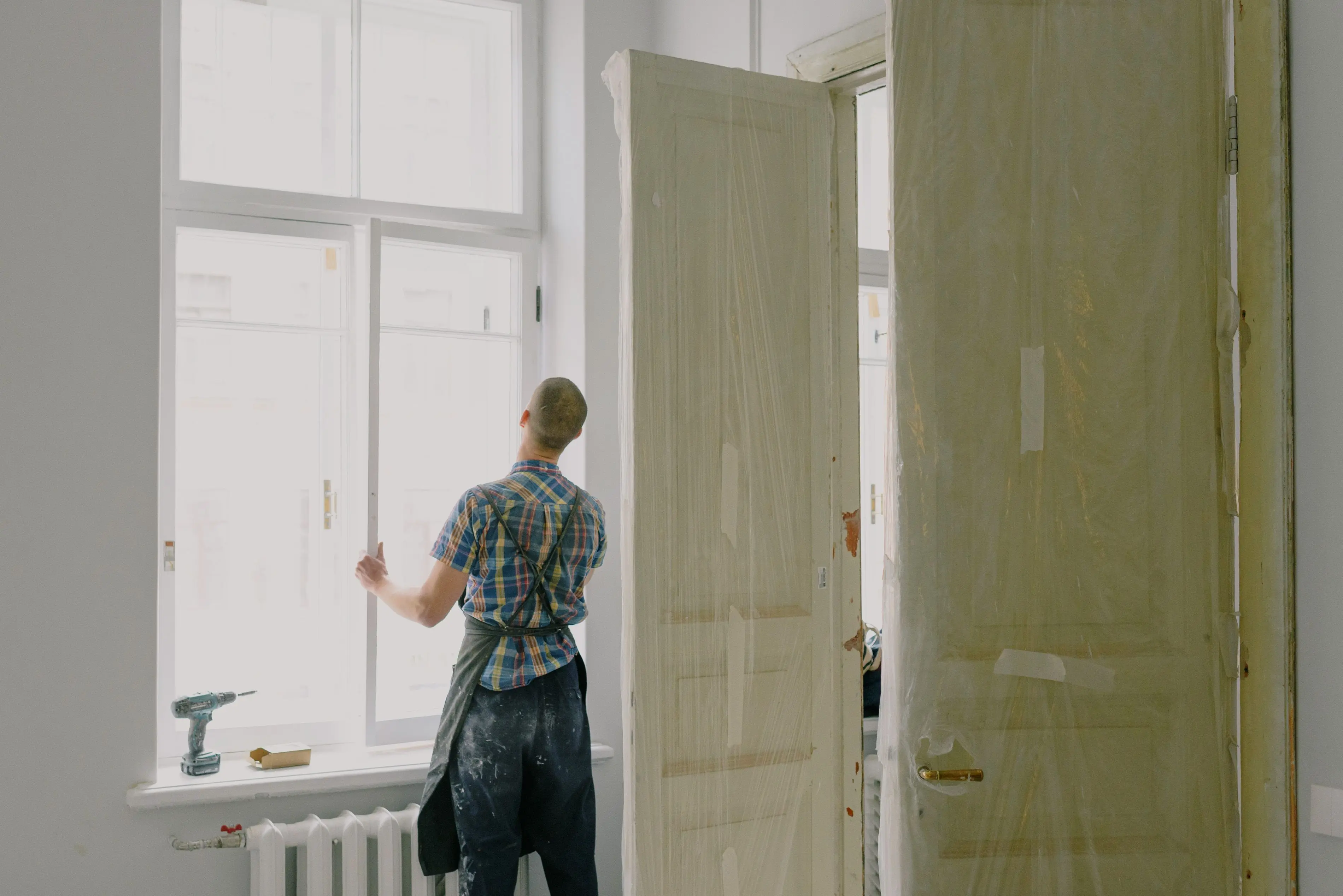 how much does it cost to reside a house Back view of unrecognizable workman in apron mounting window near drilling machine and doors in flat