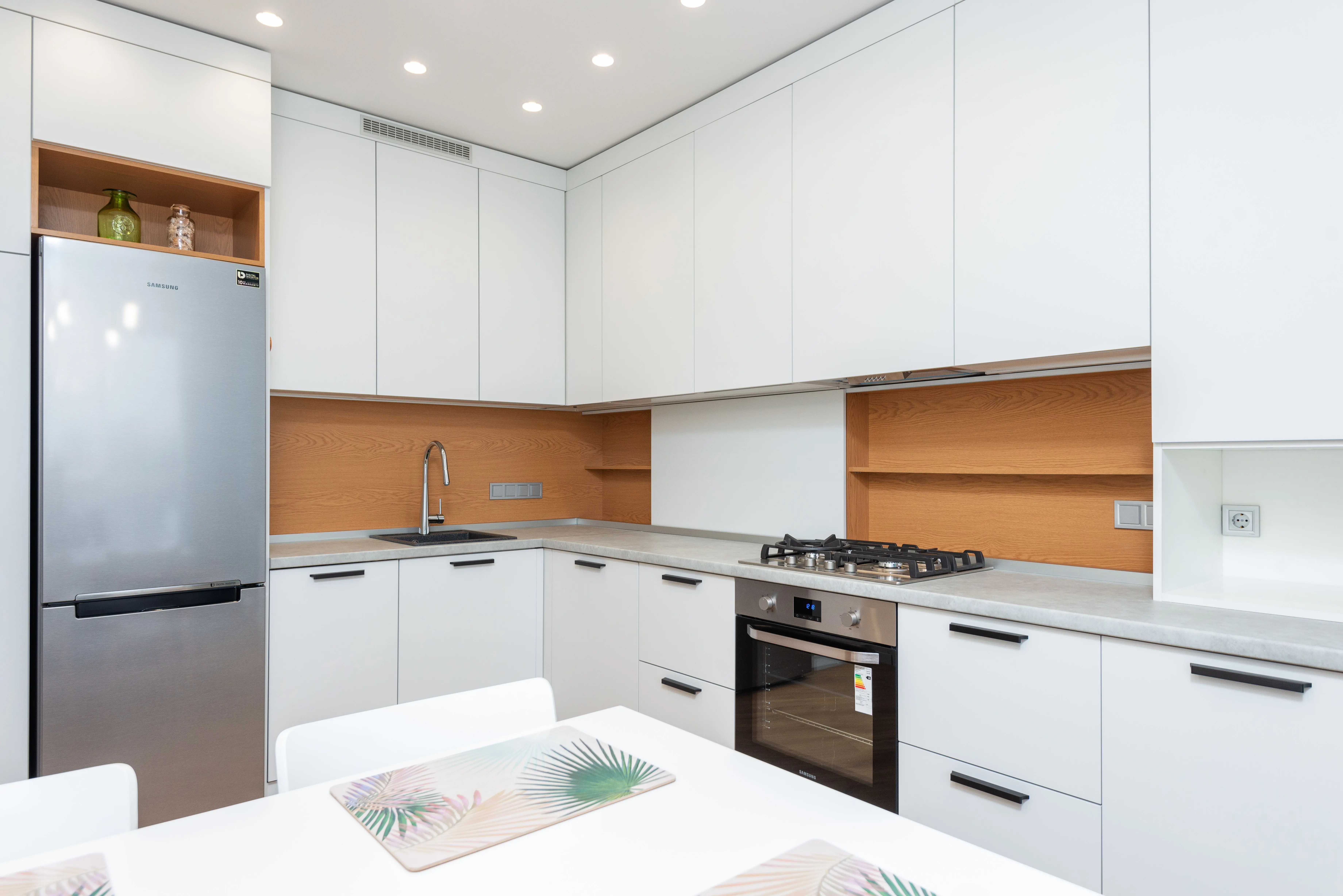white shaker kitchen cabinets Contemporary kitchen with gas stove and oven against table with placemats and refrigerator reflecting shiny lamps in house