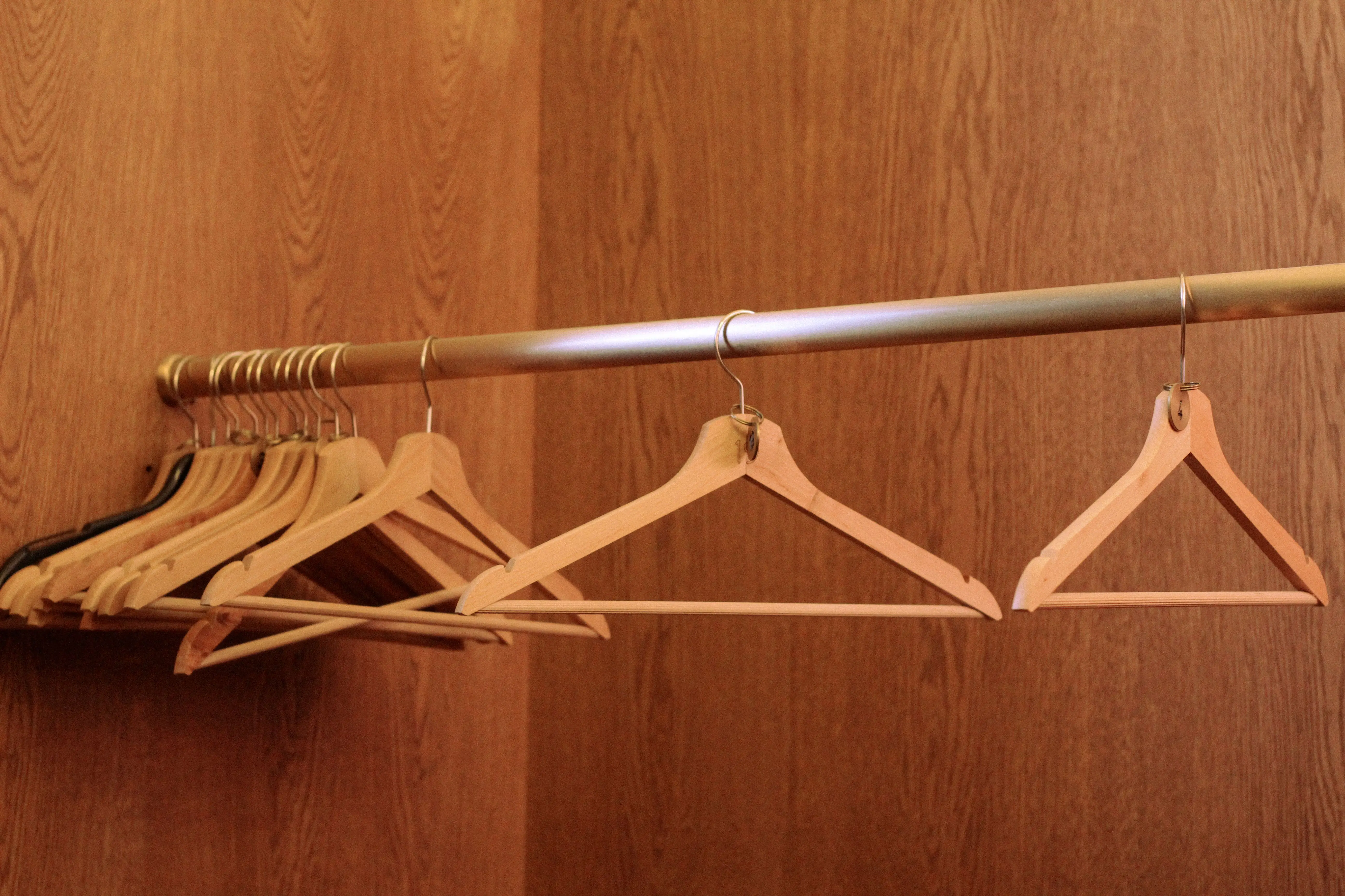 heavy duty closet rod A row of wooden hangers on a metal rod in an empty, wood-paneled closet.