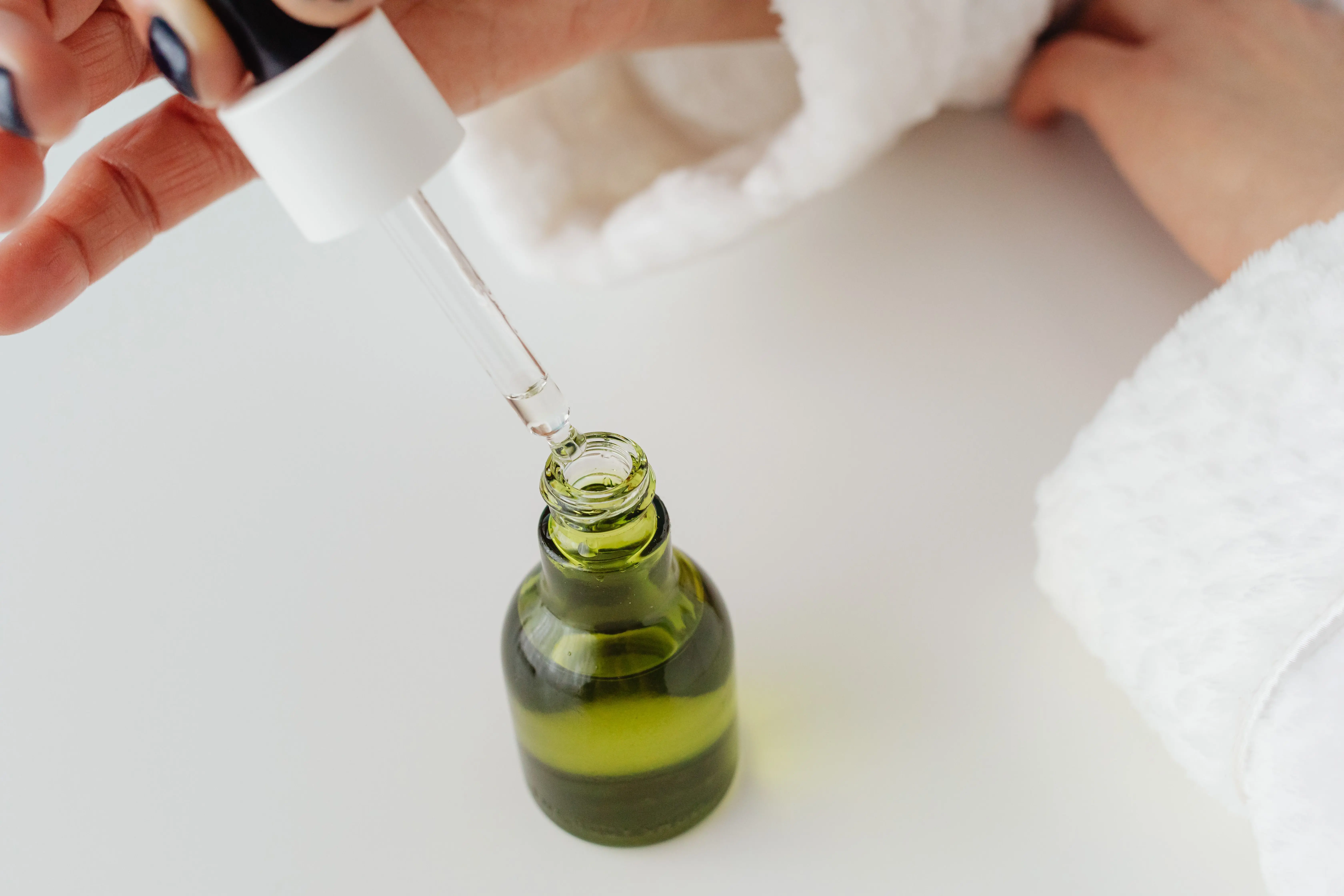 what scent do flies hate Close-up of hands with manicured nails holding a dropper over a green serum bottle.
