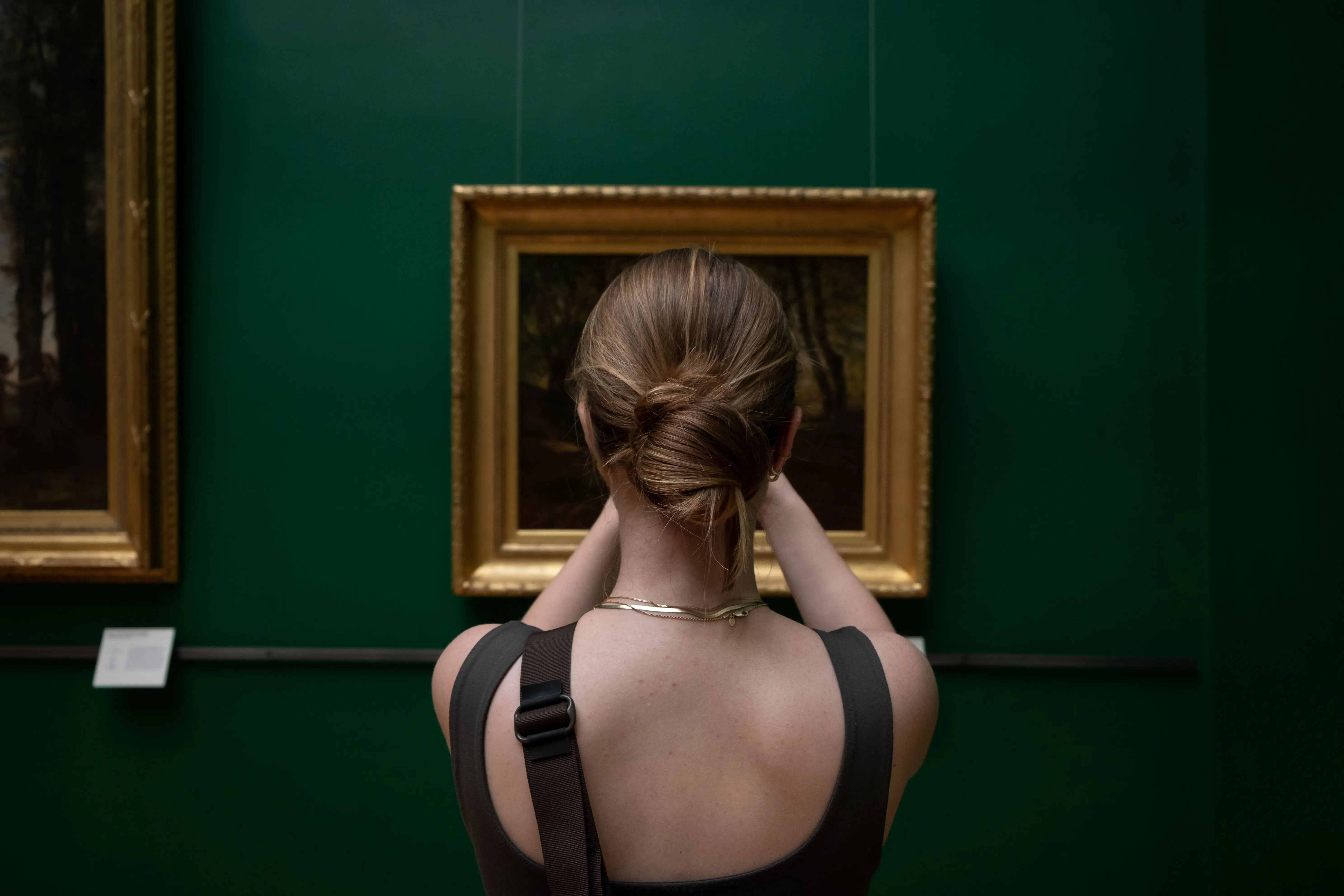 gold wall art Back view of a woman photographing a painting in an art gallery.