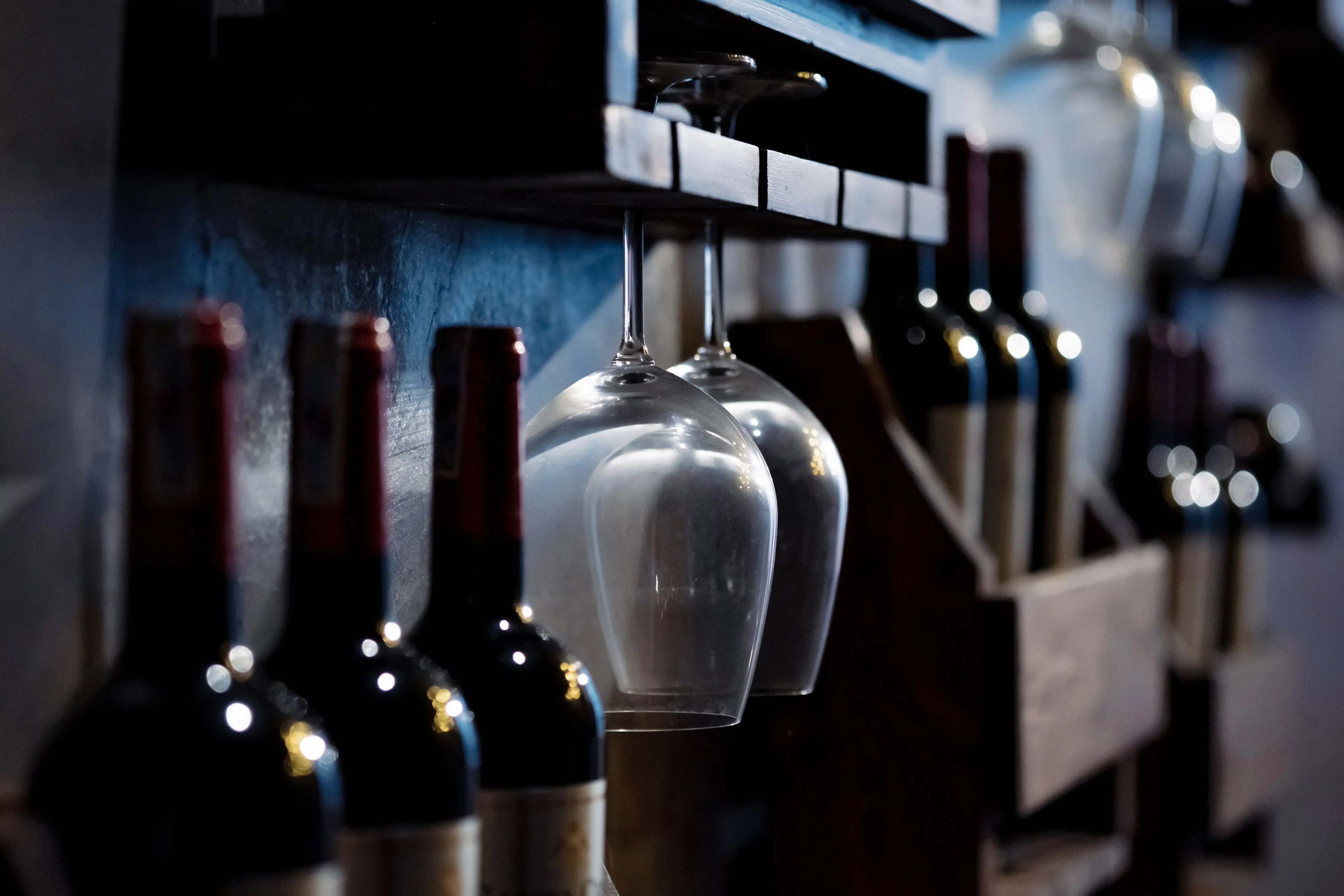 glassware storage containers Close-up of wine bottles and glasses on wooden shelves in a dimly lit cellar, creating a cozy ambiance.