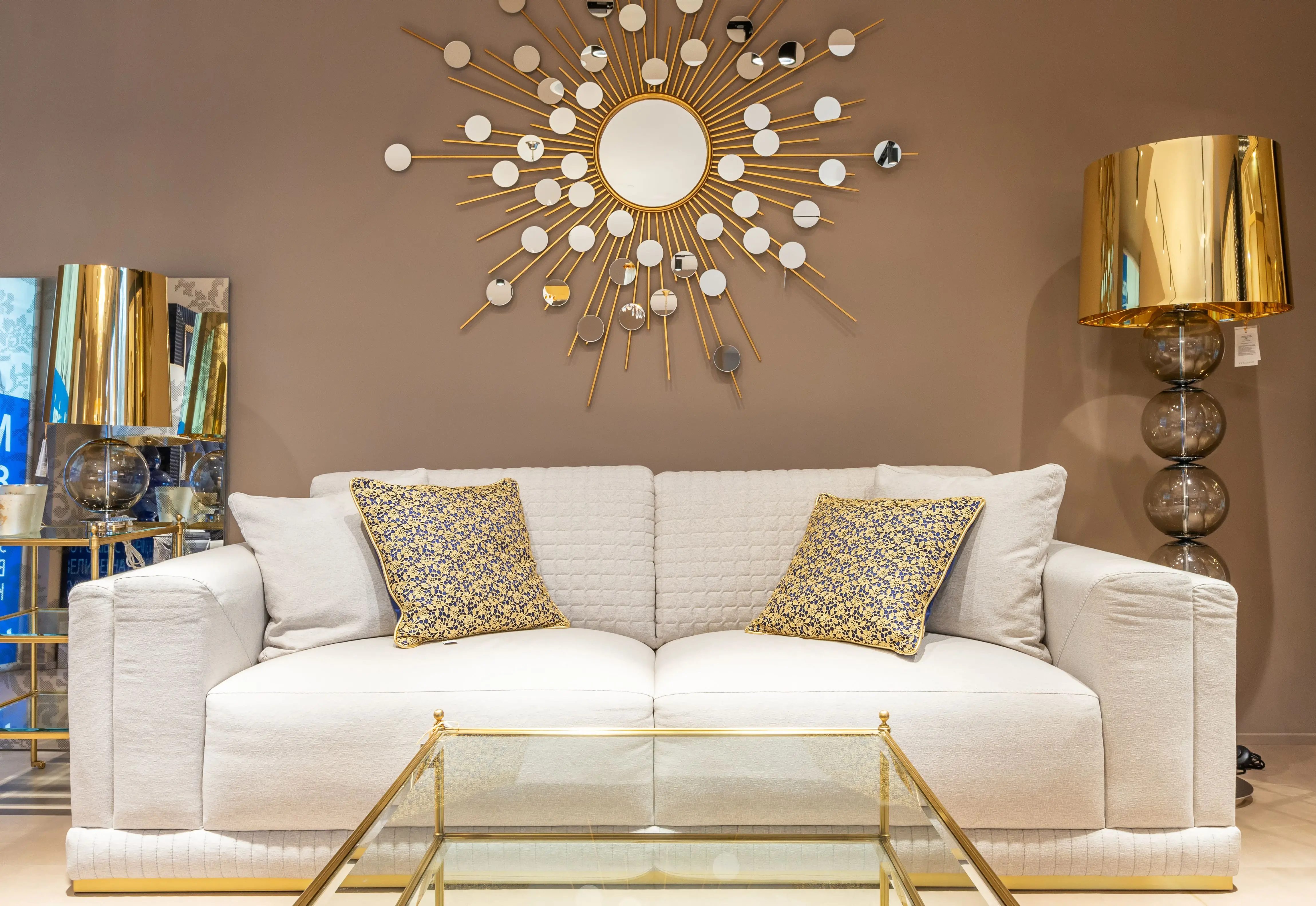 gold wall art Comfortable white sofa with pillows placed near with floor lamp at wall with decorative elements in stylish living room of apartment