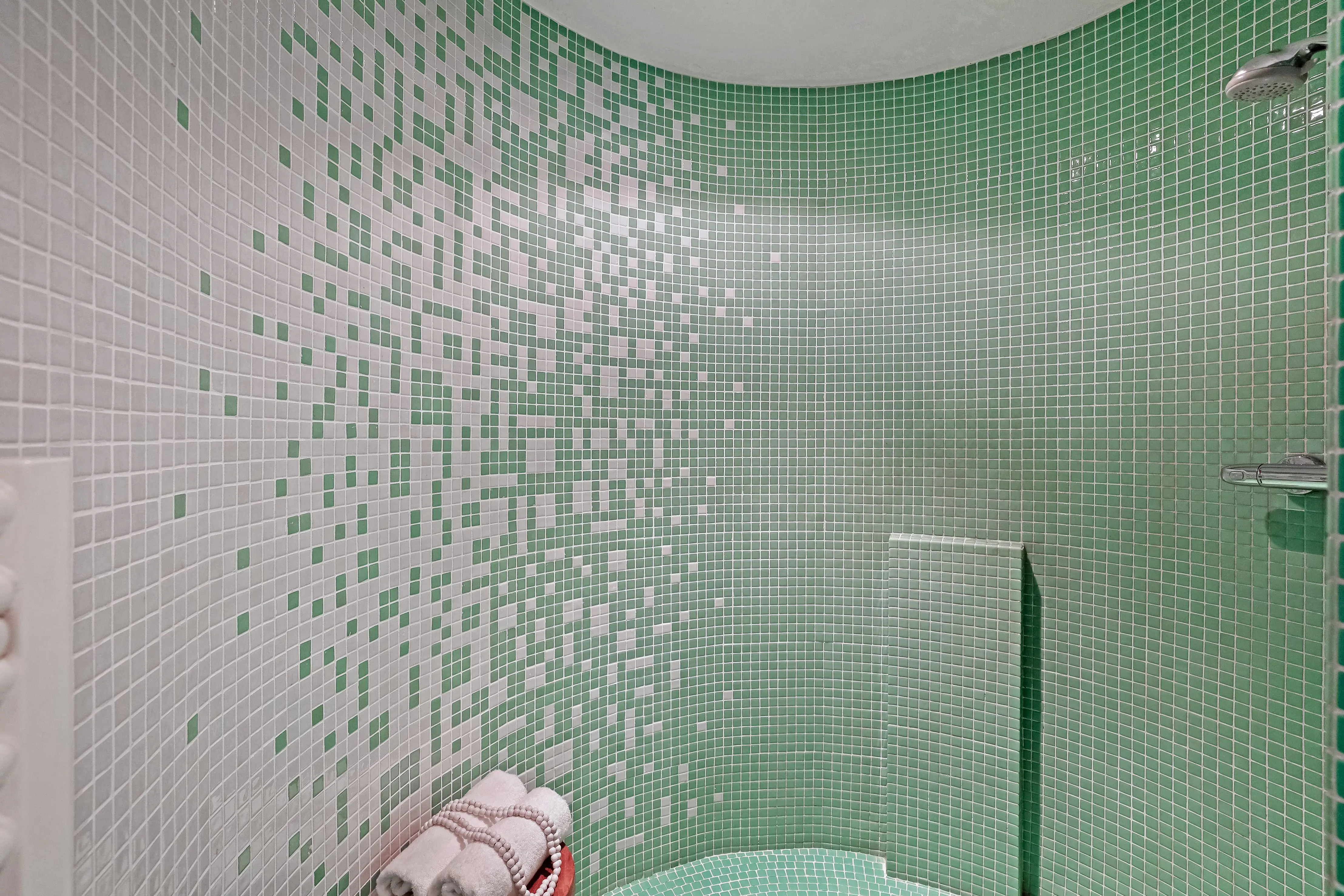 green shower tile A stylish small bathroom with green and white mosaic tiles and a neatly folded towel set.
