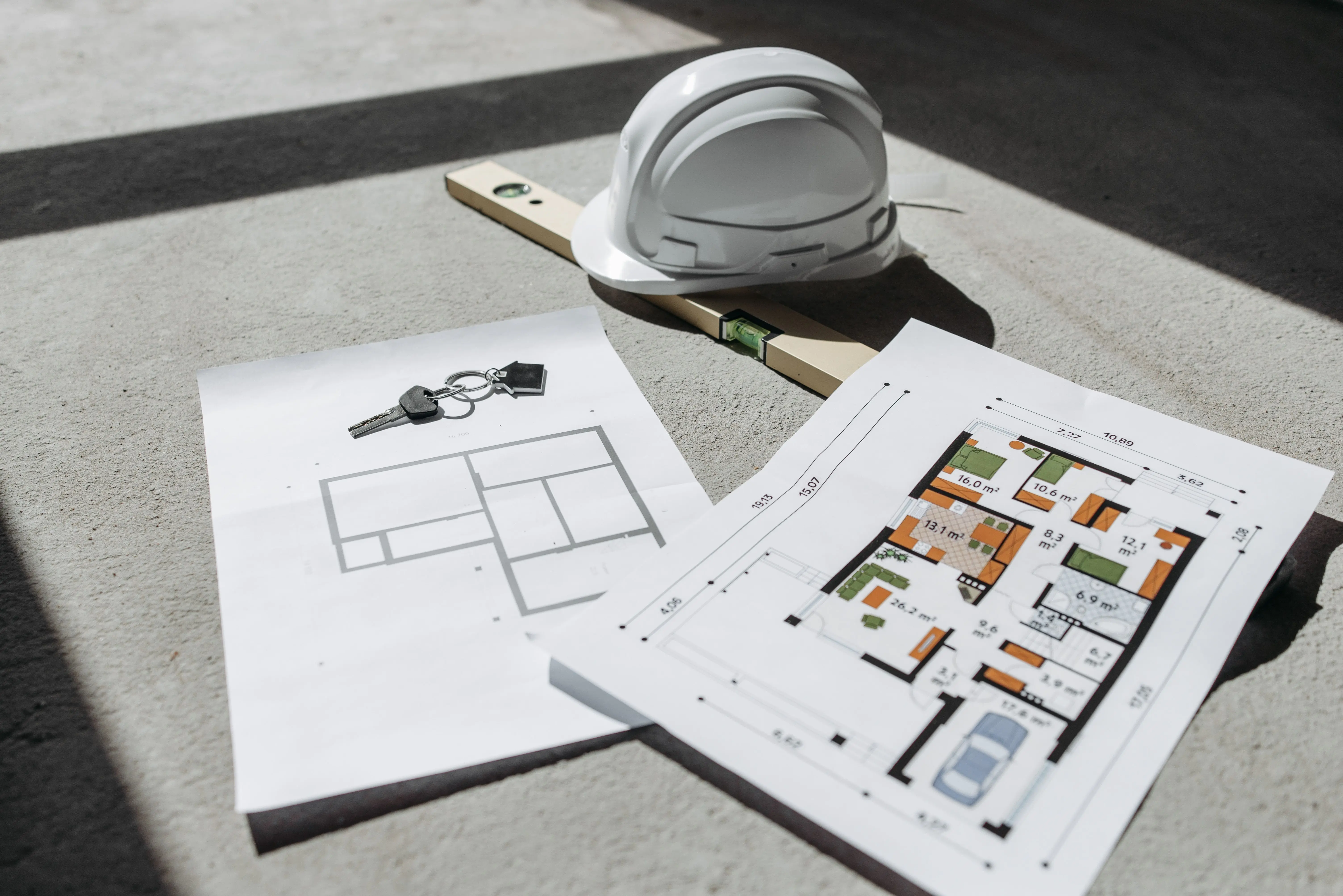 house addition cost Architectural floor plans with helmet and keys on sunlit floor, perfect for real estate or construction themes.