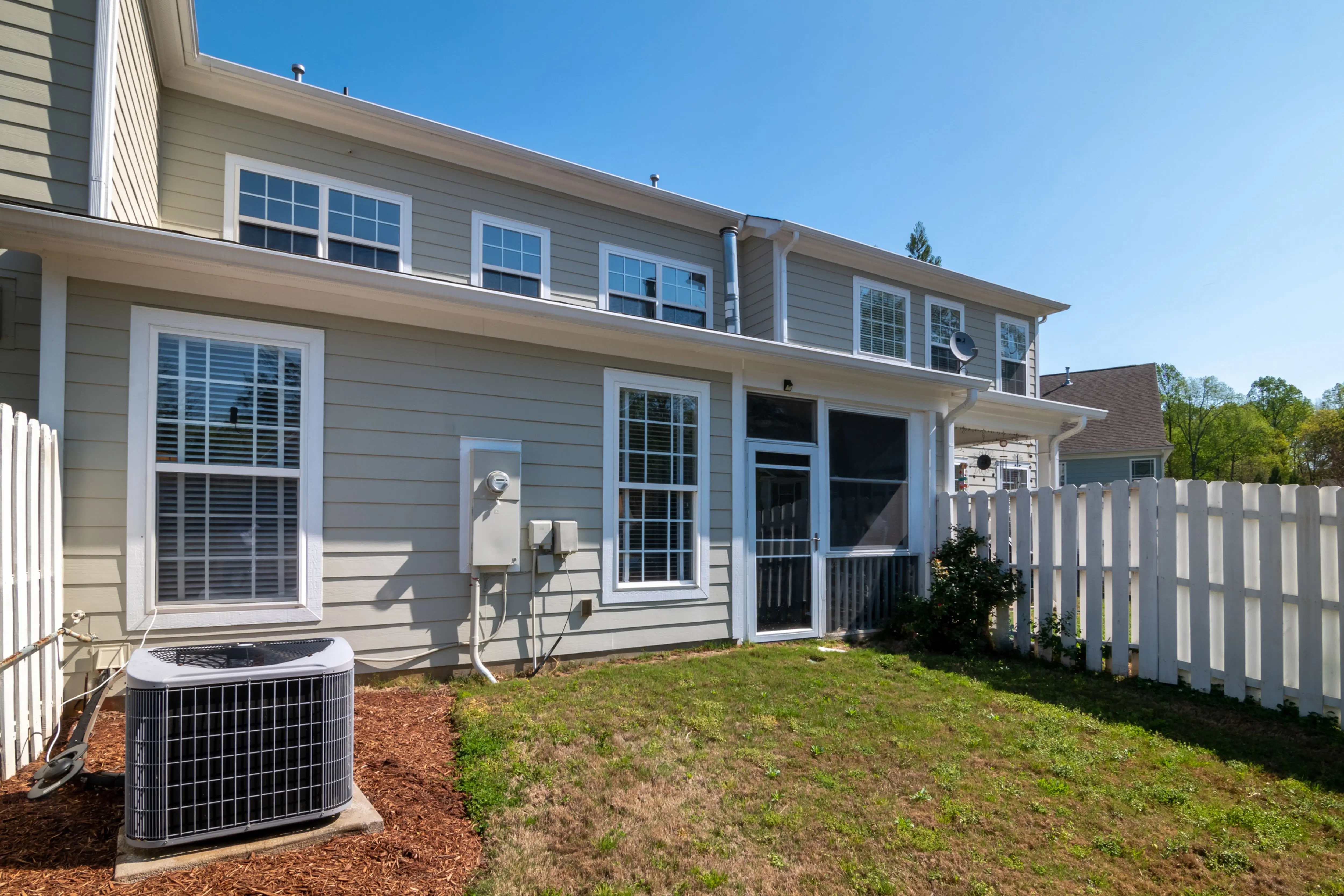 how much does it cost to reside a house A sunlit backyard view of a modern grey house with white fencing and AC unit.