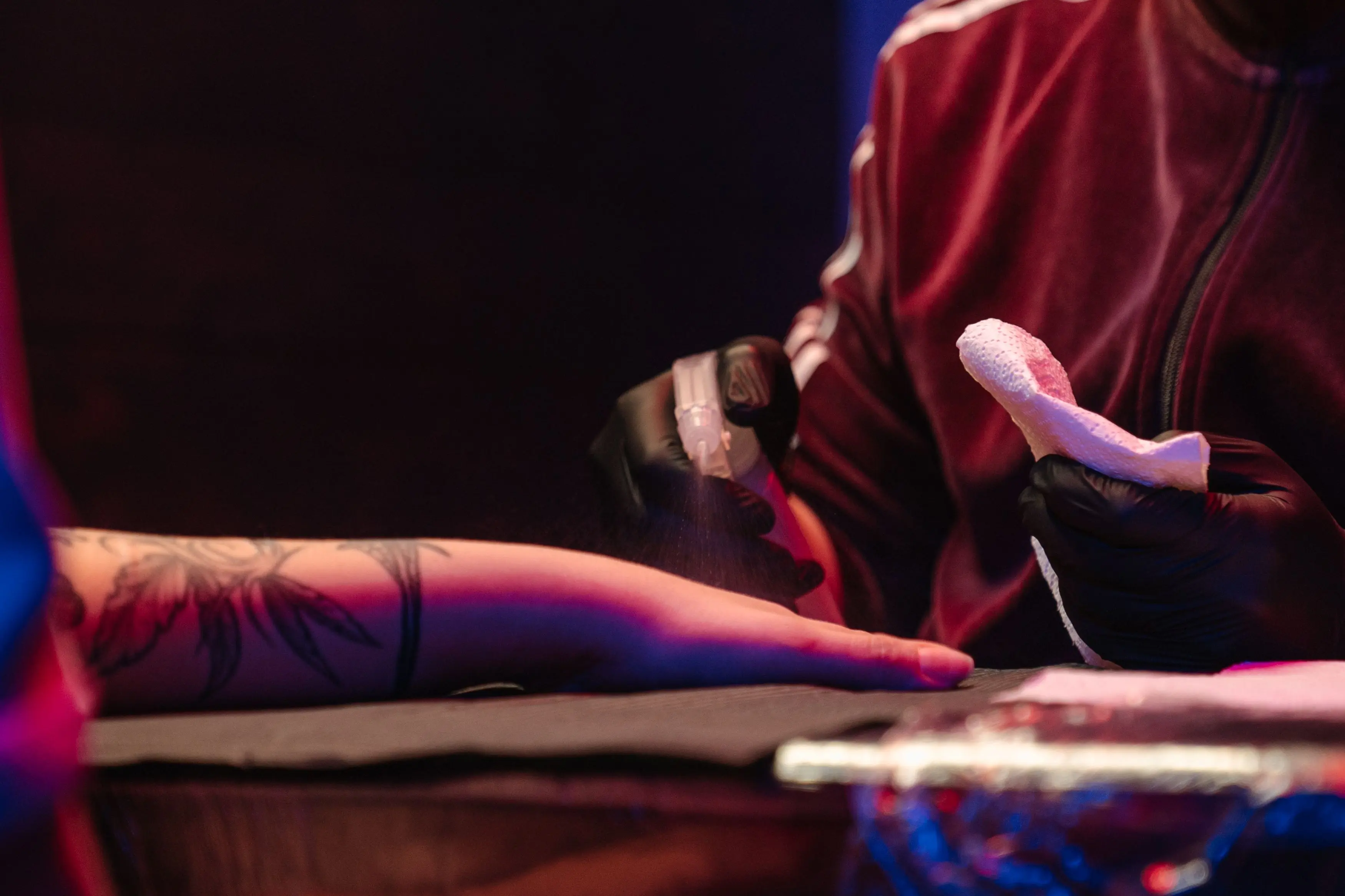 ink remover Tattoo artist cleaning client's arm before tattooing in studio with neon lights.