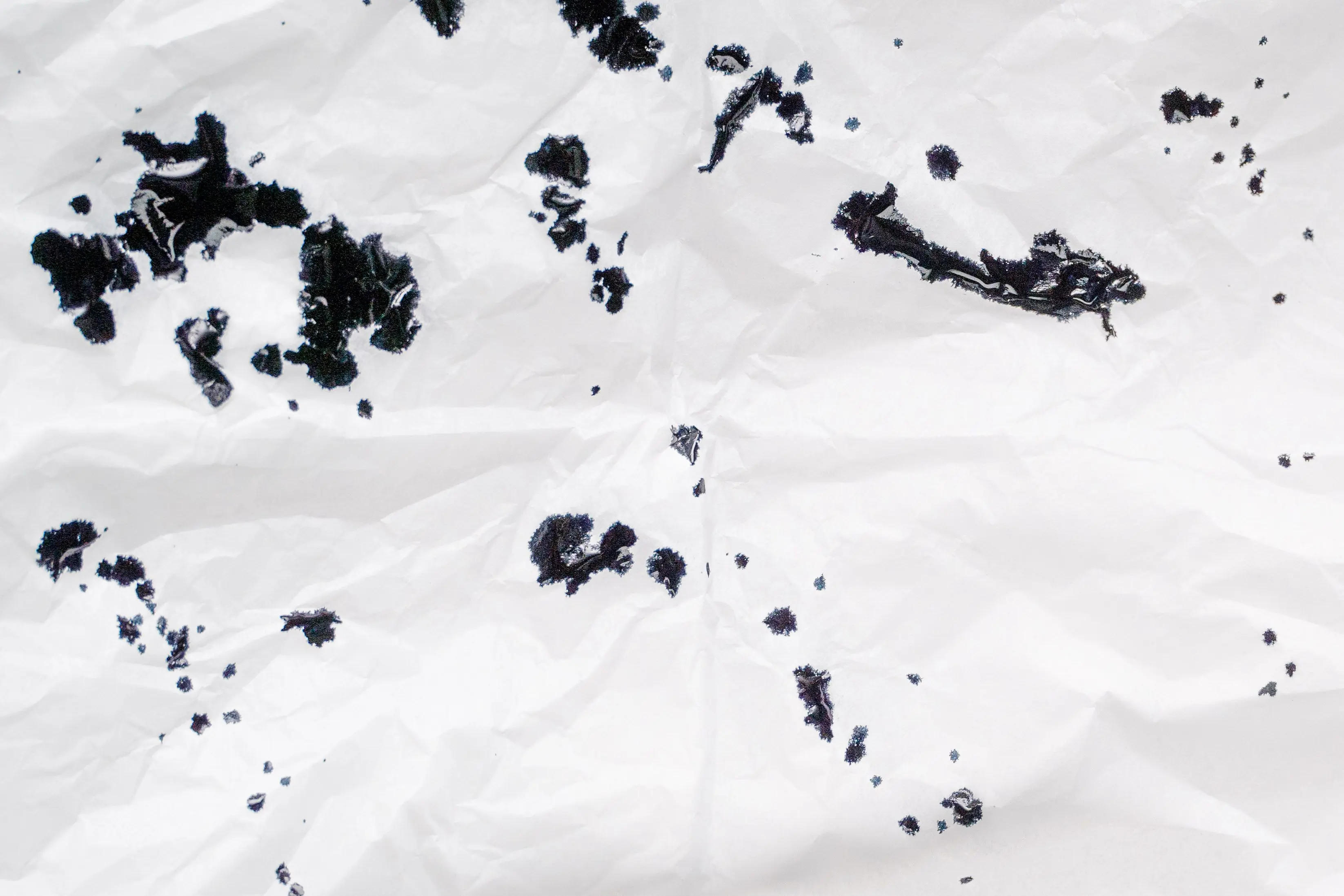 ink remover Crumpled white paper with scattered black ink spots creating an abstract pattern.