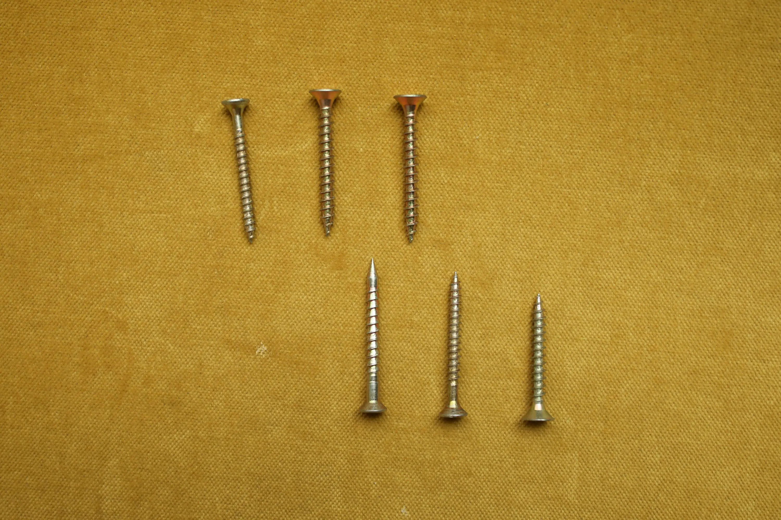 metal desk legs A close-up of seven silver screws arranged on a textured yellow surface.
