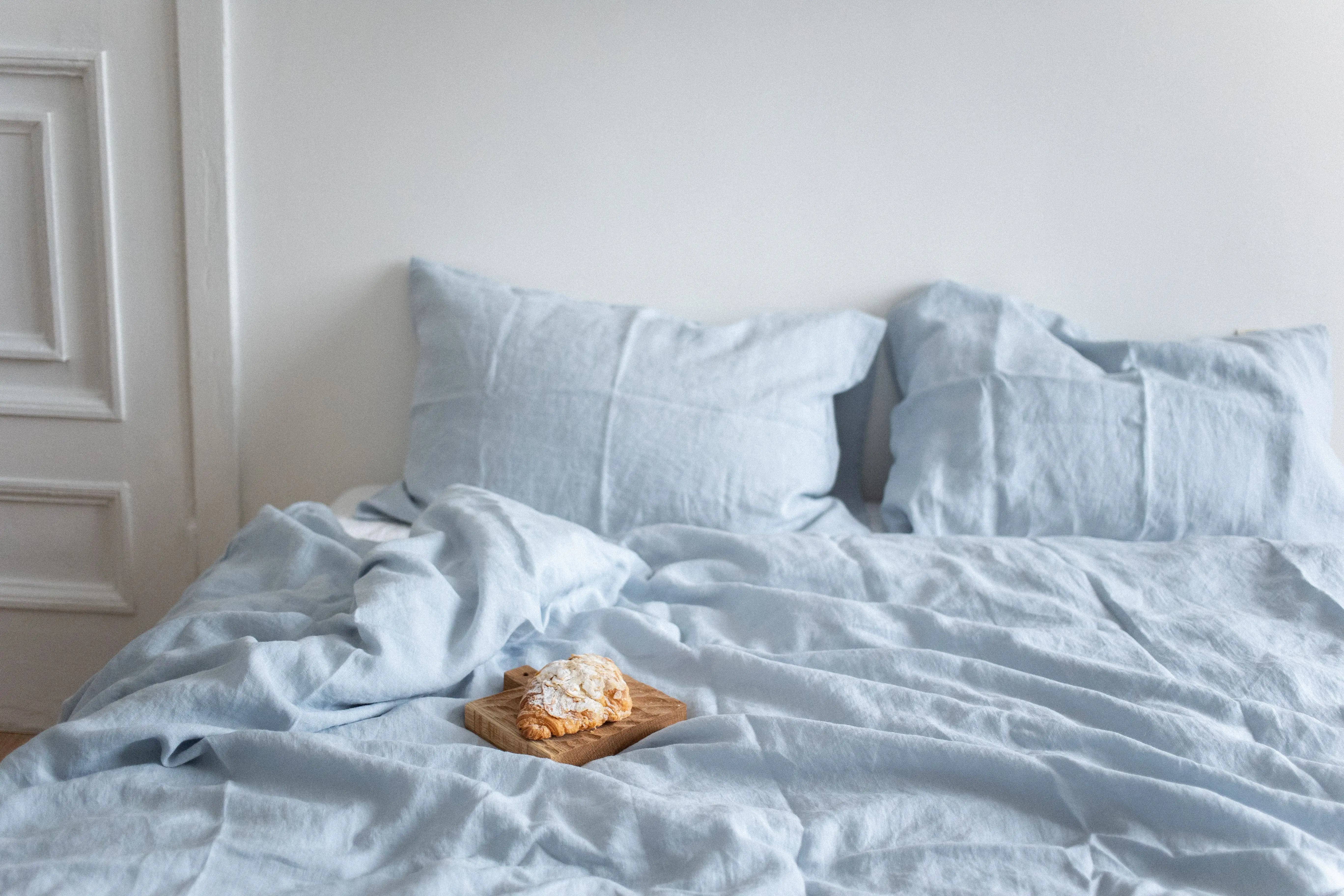 light blue throw pillows A tranquil bedroom scene featuring a croissant on a light blue bed, creating a cozy and inviting ambiance.
