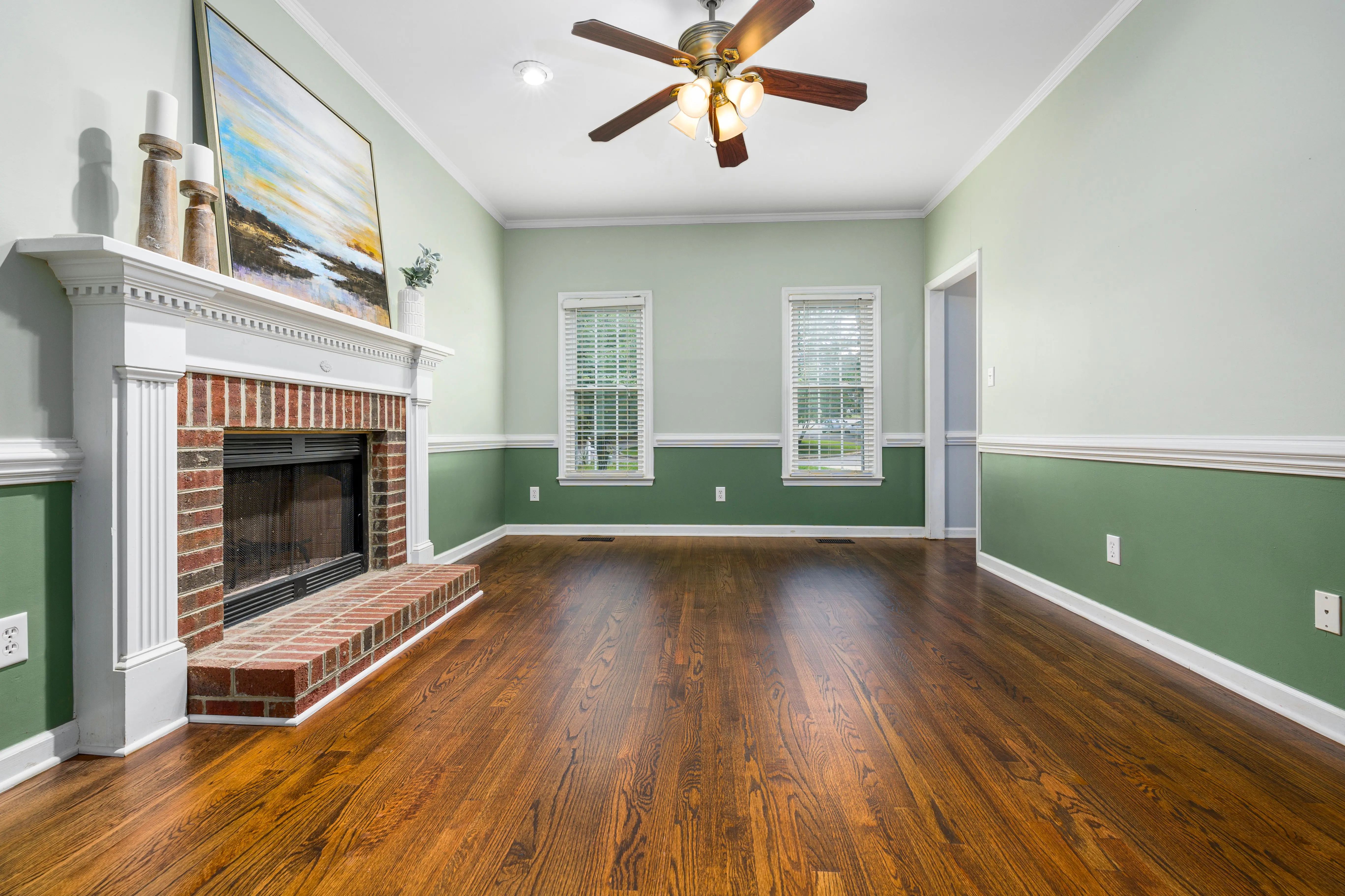 green wall paint A cozy empty living room featuring a brick fireplace, wooden floors, and elegant decor.