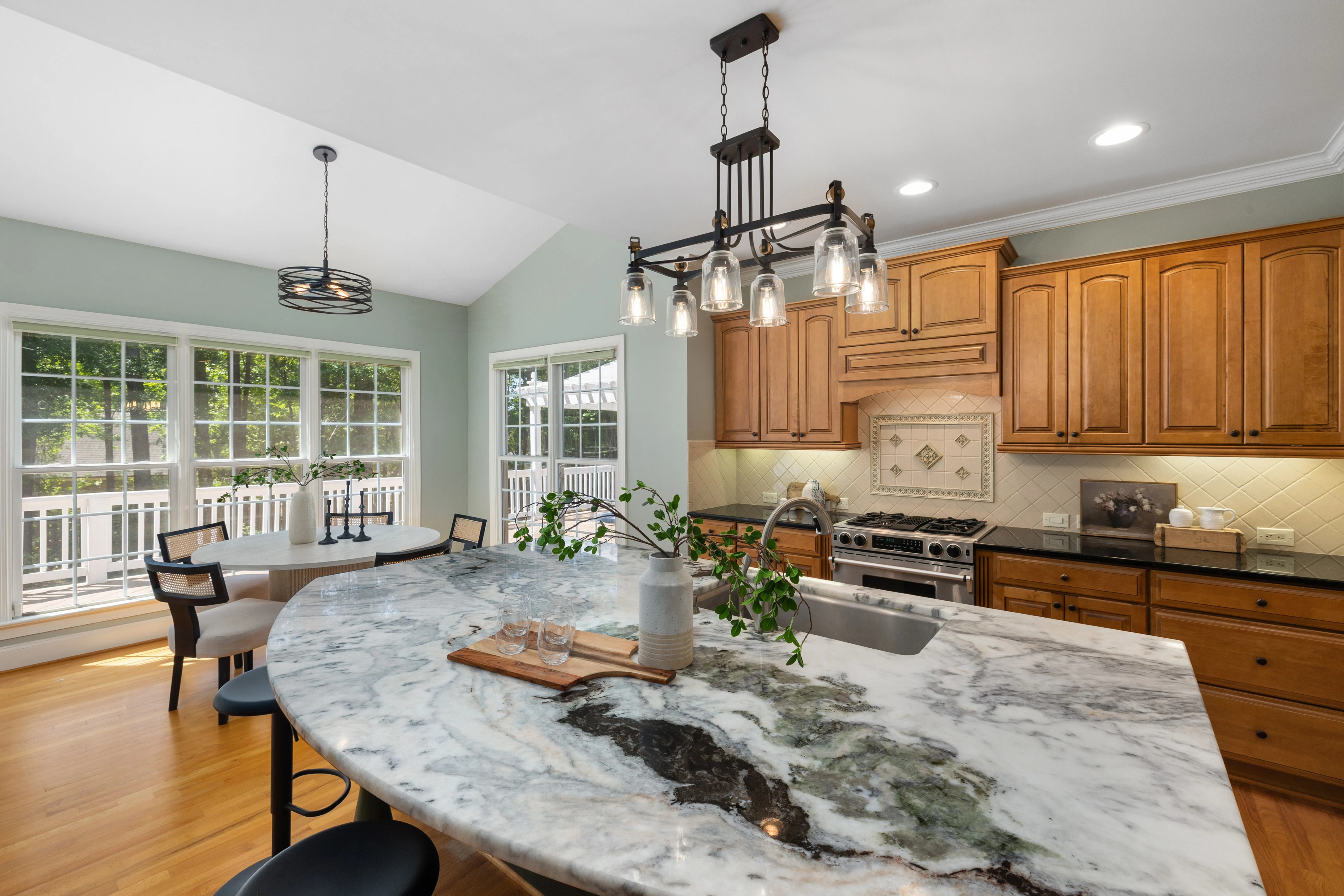 cherry wood kitchen cabinets Bright and inviting kitchen interior featuring marble countertops, wooden cabinets, and large windows.