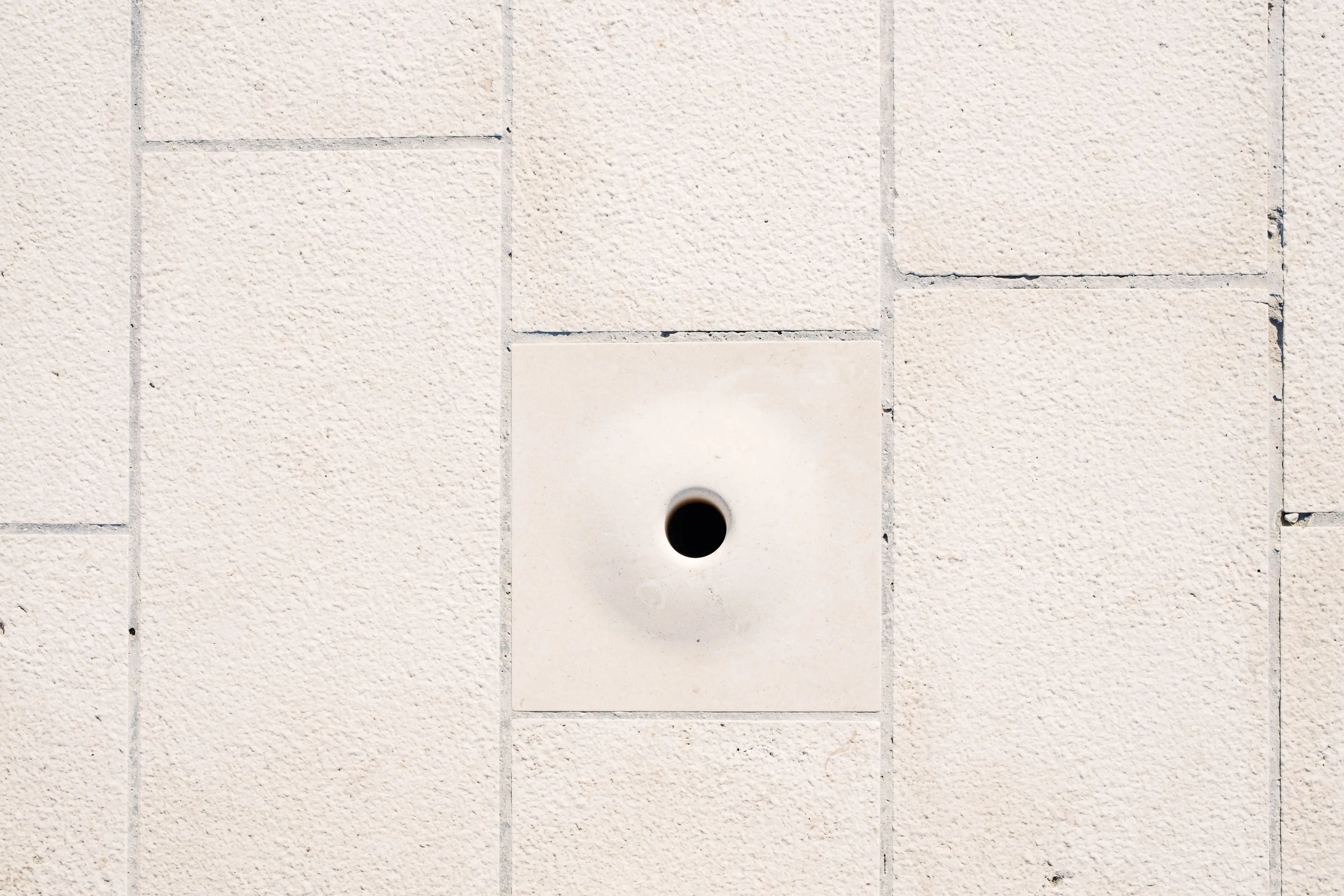 mouse in wall Close-up of a minimalist white brick wall featuring a central circular hole.
