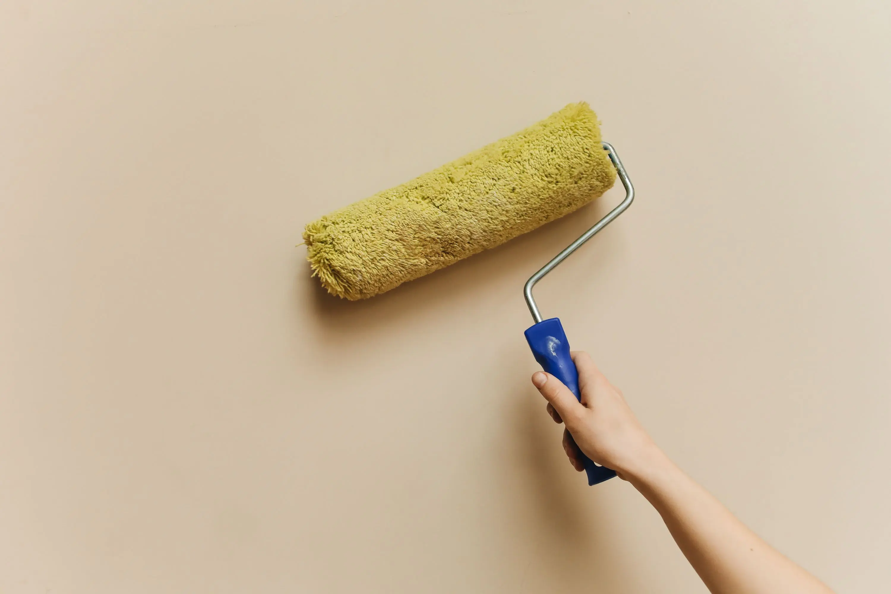green wall paint A hand using a yellow paint roller to paint a beige wall. Perfect for DIY and home improvement themes.