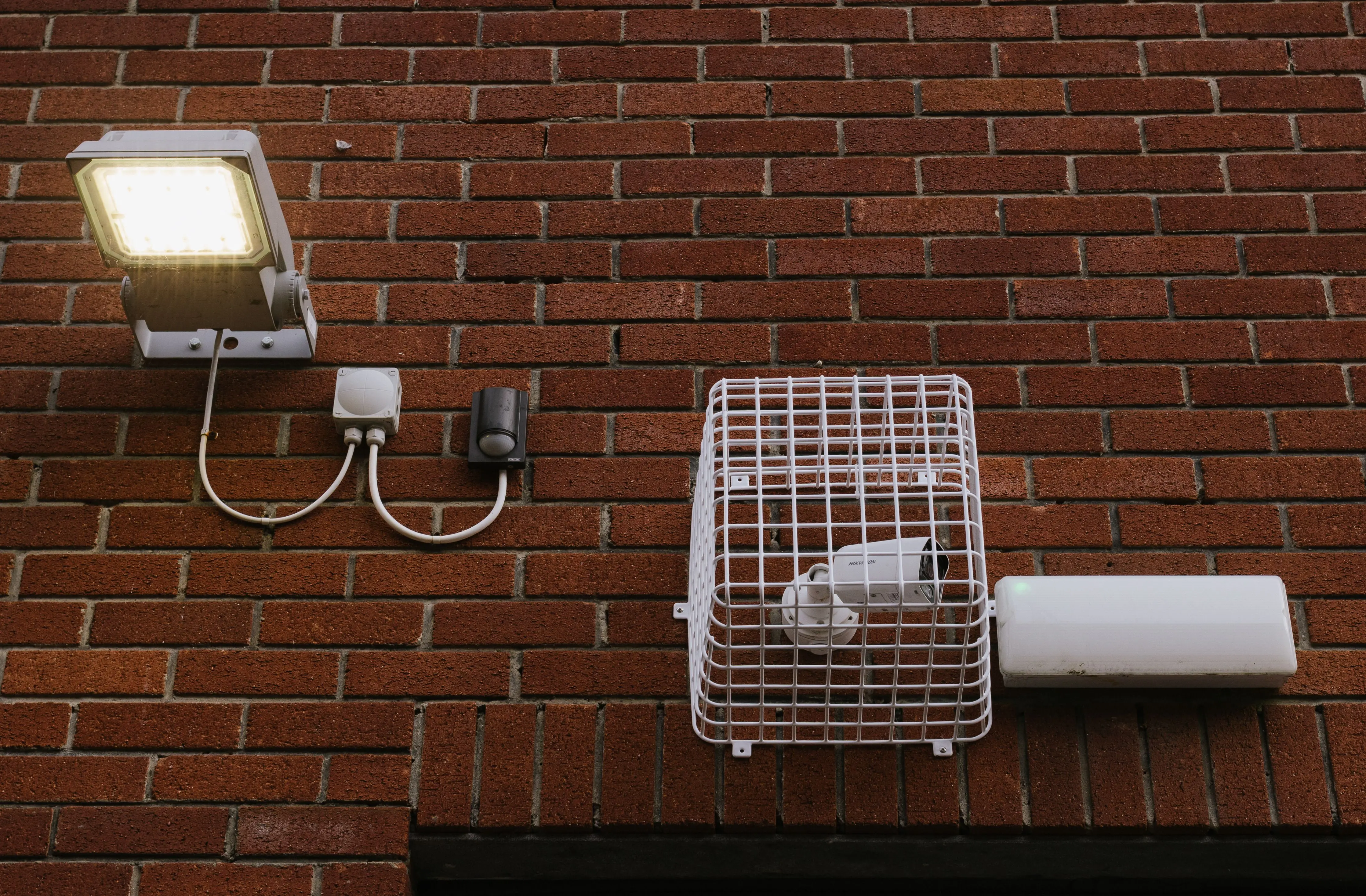 outdoor path lights Close-up view of a brick wall featuring a LED light and a caged security camera.